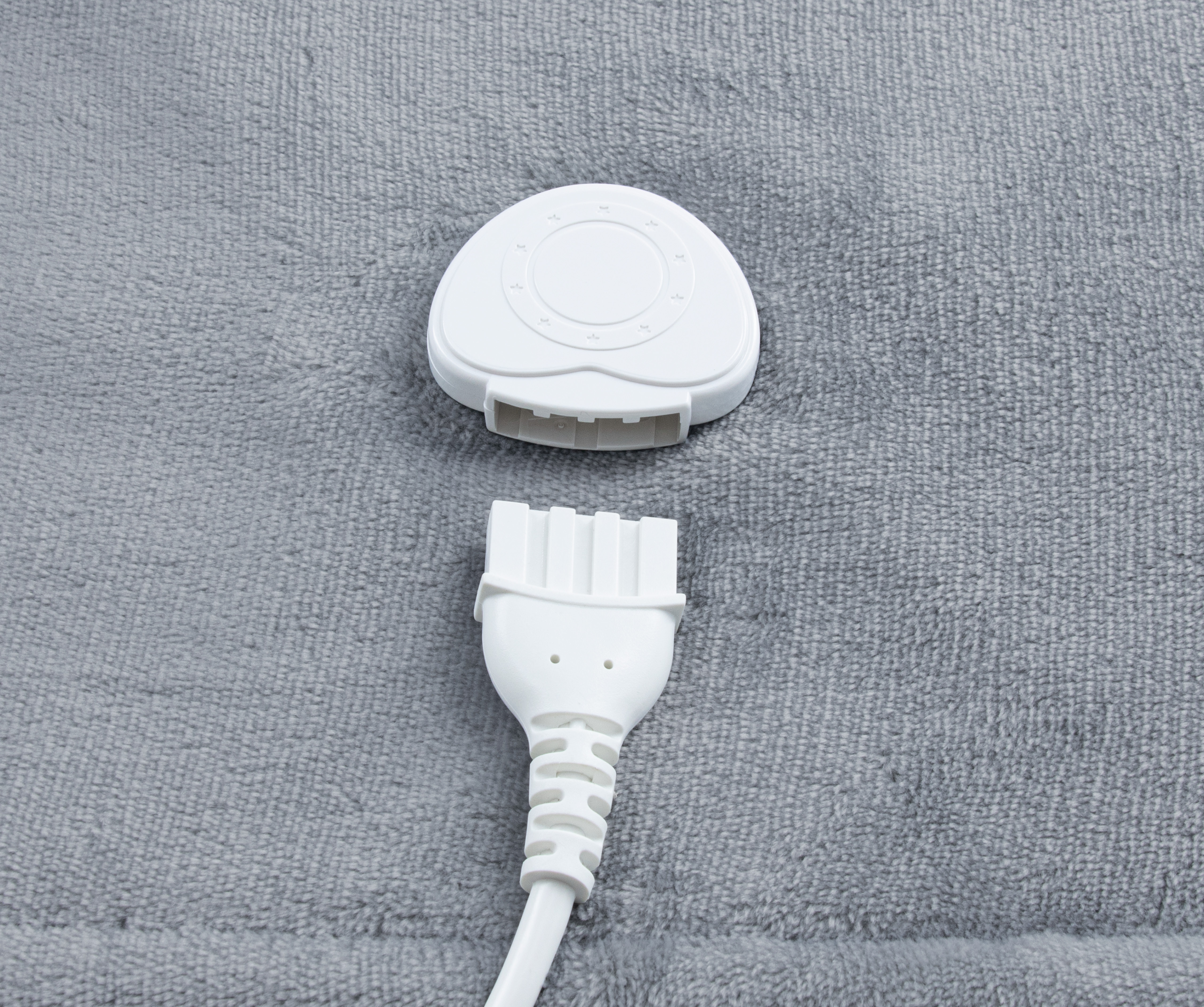 Weißer Regler und Stecker auf grauer Stoffoberfläche.