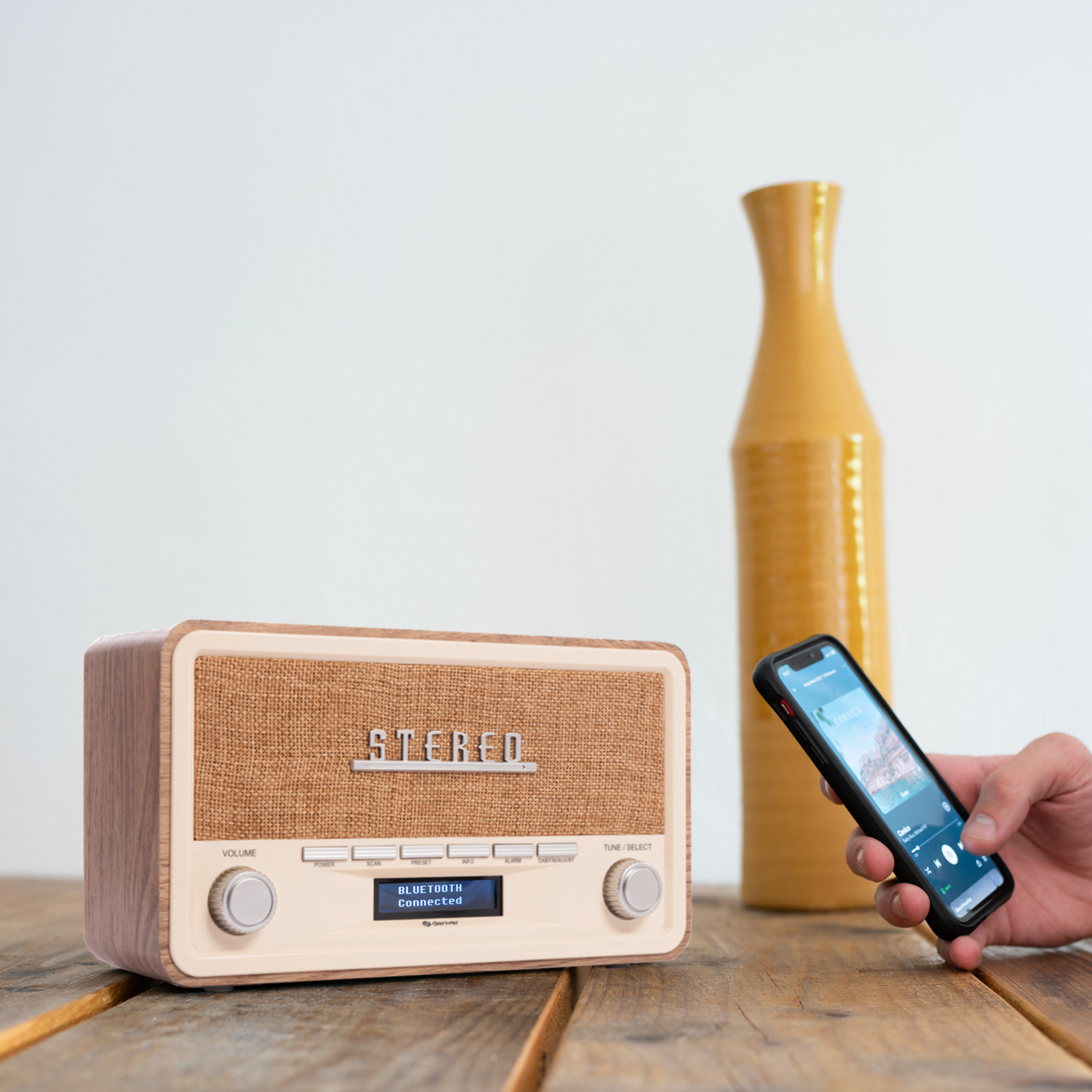 Retro radio with wooden finish, phone playing music, and a yellow vase.