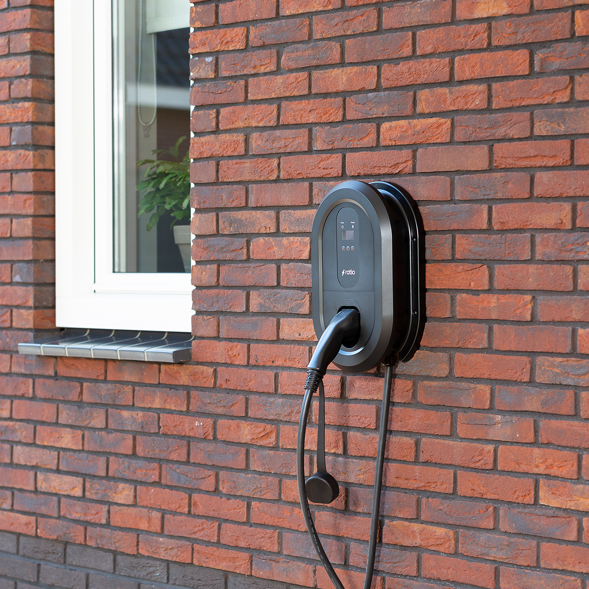 Black charging station mounted on a brick wall, with charging cable and plug.