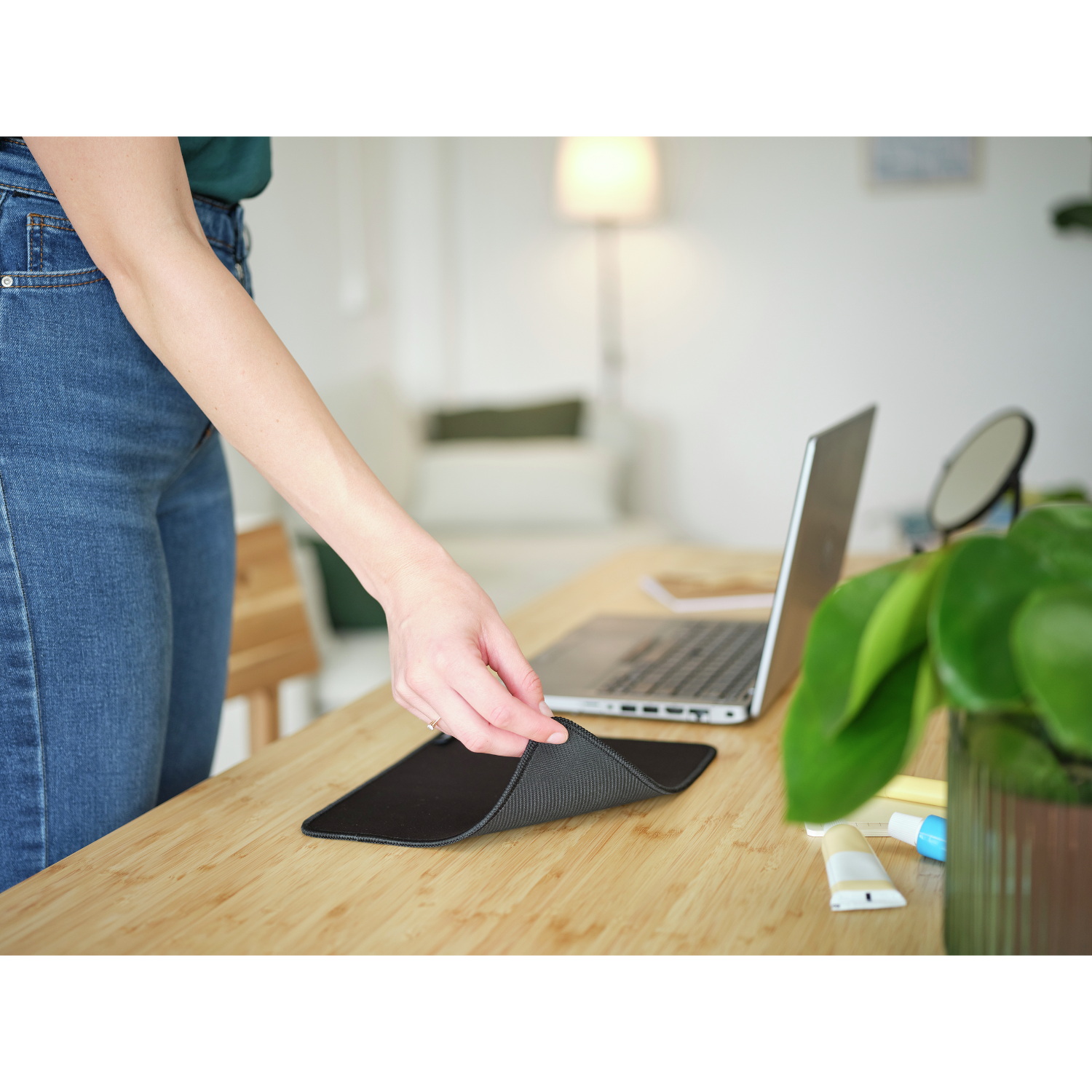 Mano che tiene un tappetino per mouse nero su un tavolo di legno. Laptop e pianta sullo sfondo.