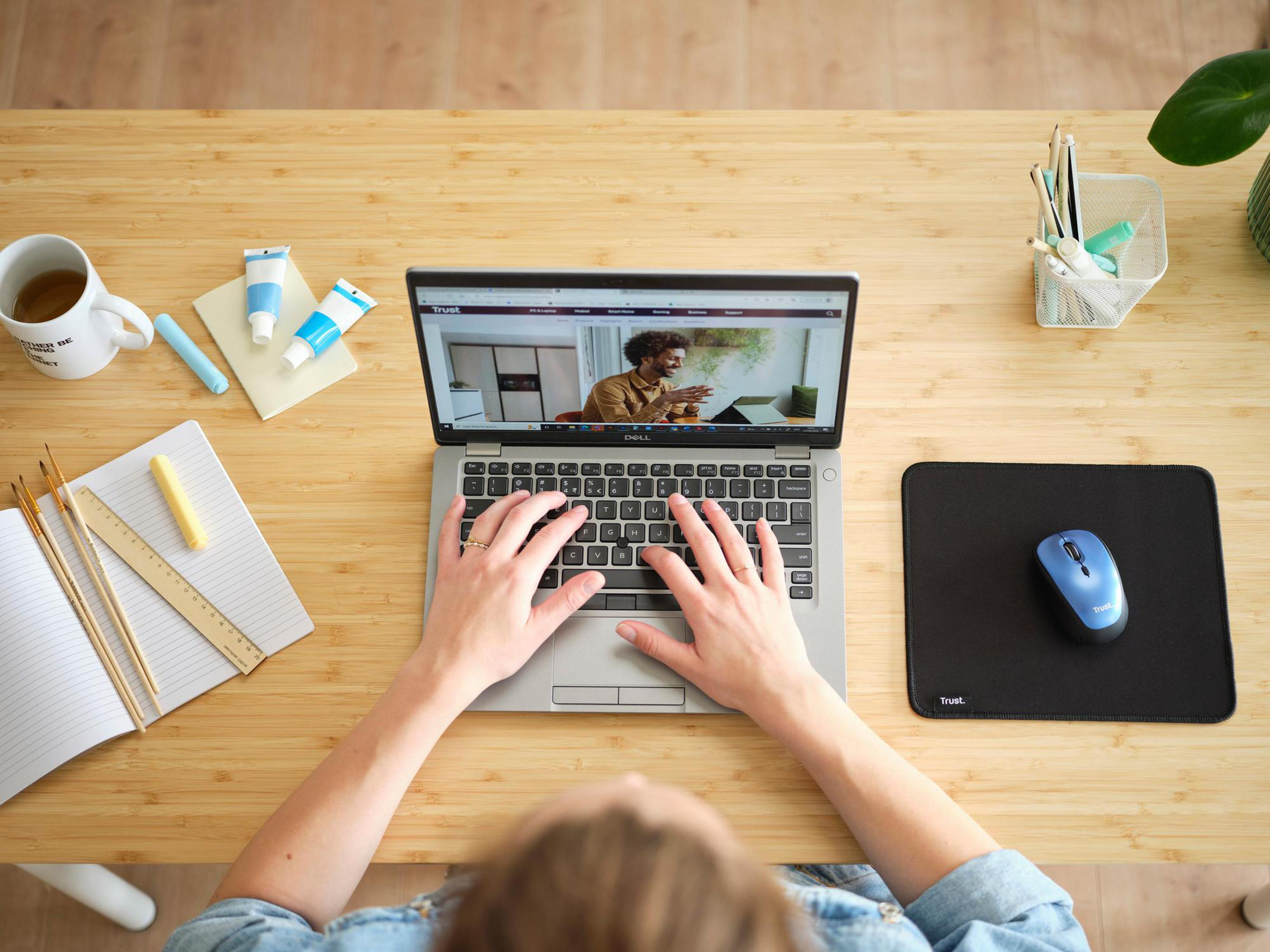Vista dall'alto di una persona che utilizza un laptop su una scrivania di legno con forniture artistiche e una tazza.