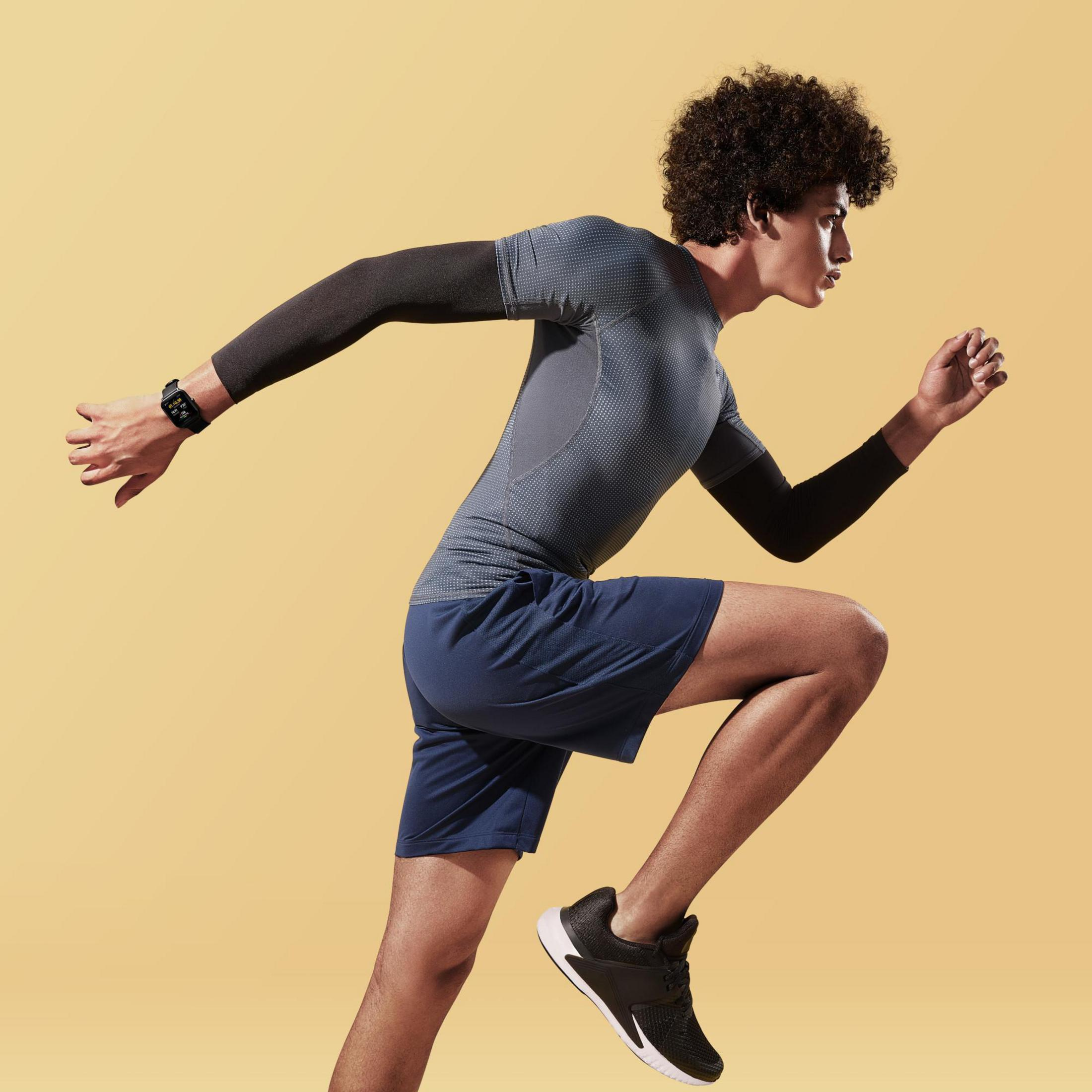 Uomo che corre in abbigliamento sportivo. Sfondo giallo. Maniche e pantaloncini neri. Smartwatch.