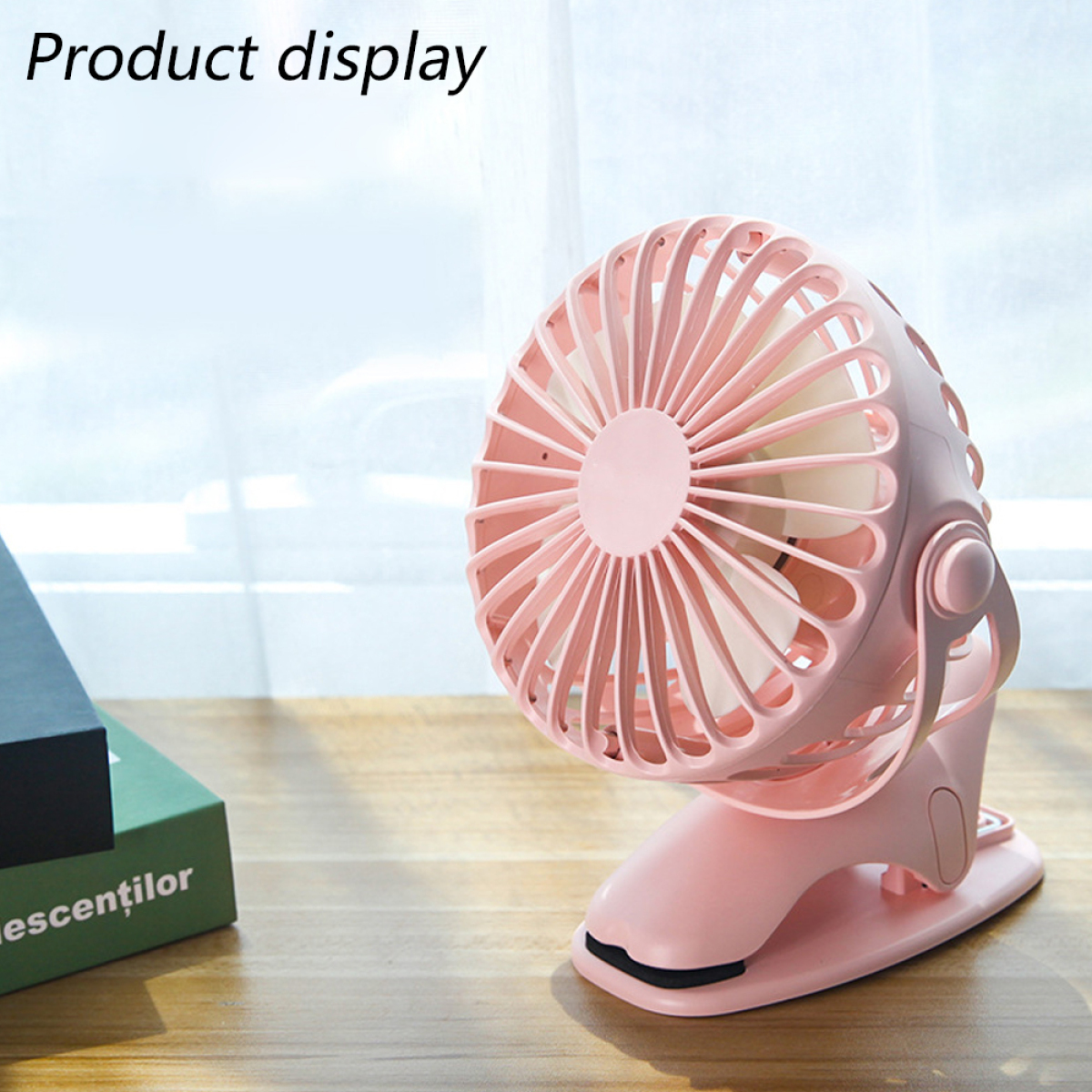 Ein rosa Mini-Ventilator in einem Clip, mit einem grünen Buch im Hintergrund.