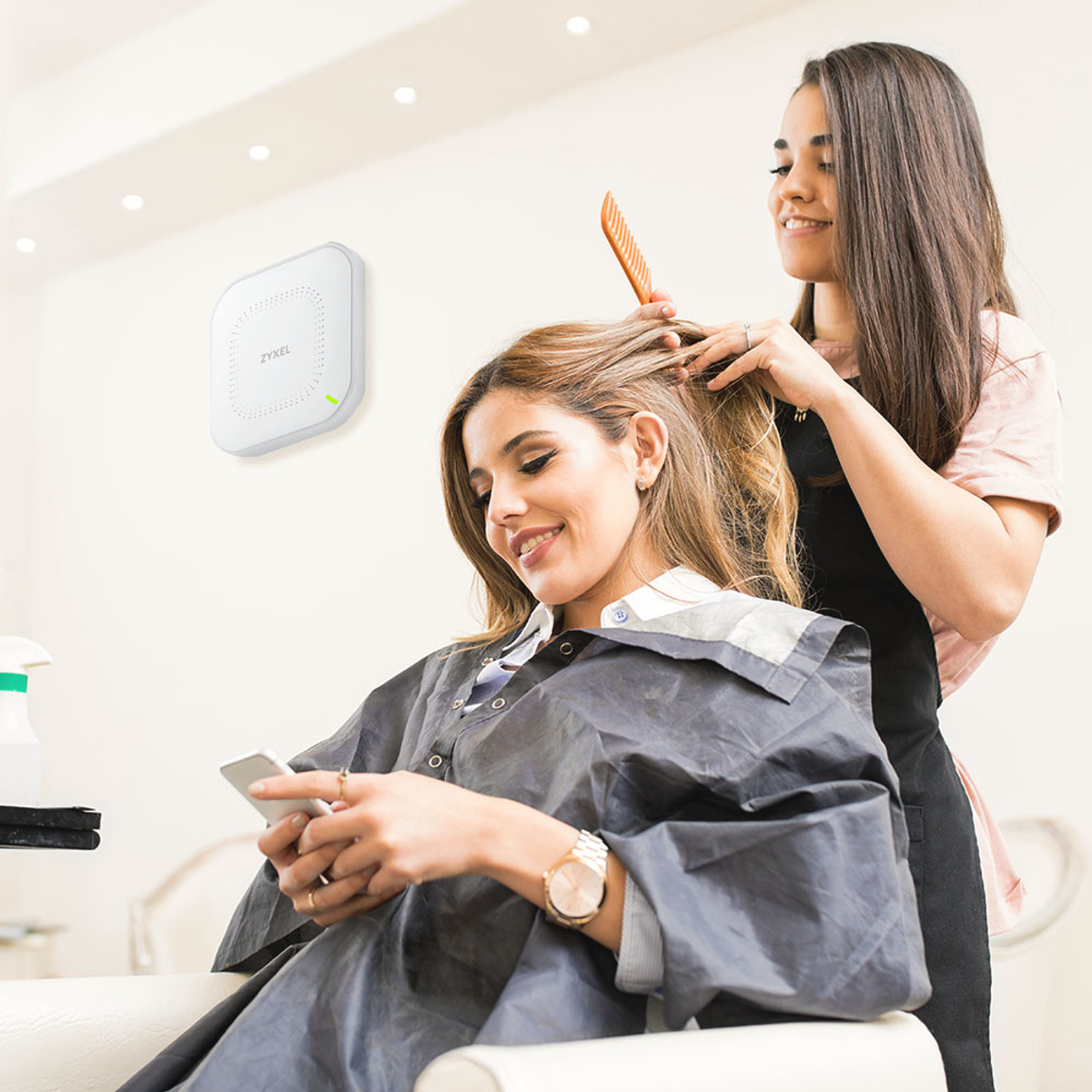 Kobieta w salonie, stylizująca włosy z punktem dostępowym Zyxel na ścianie.