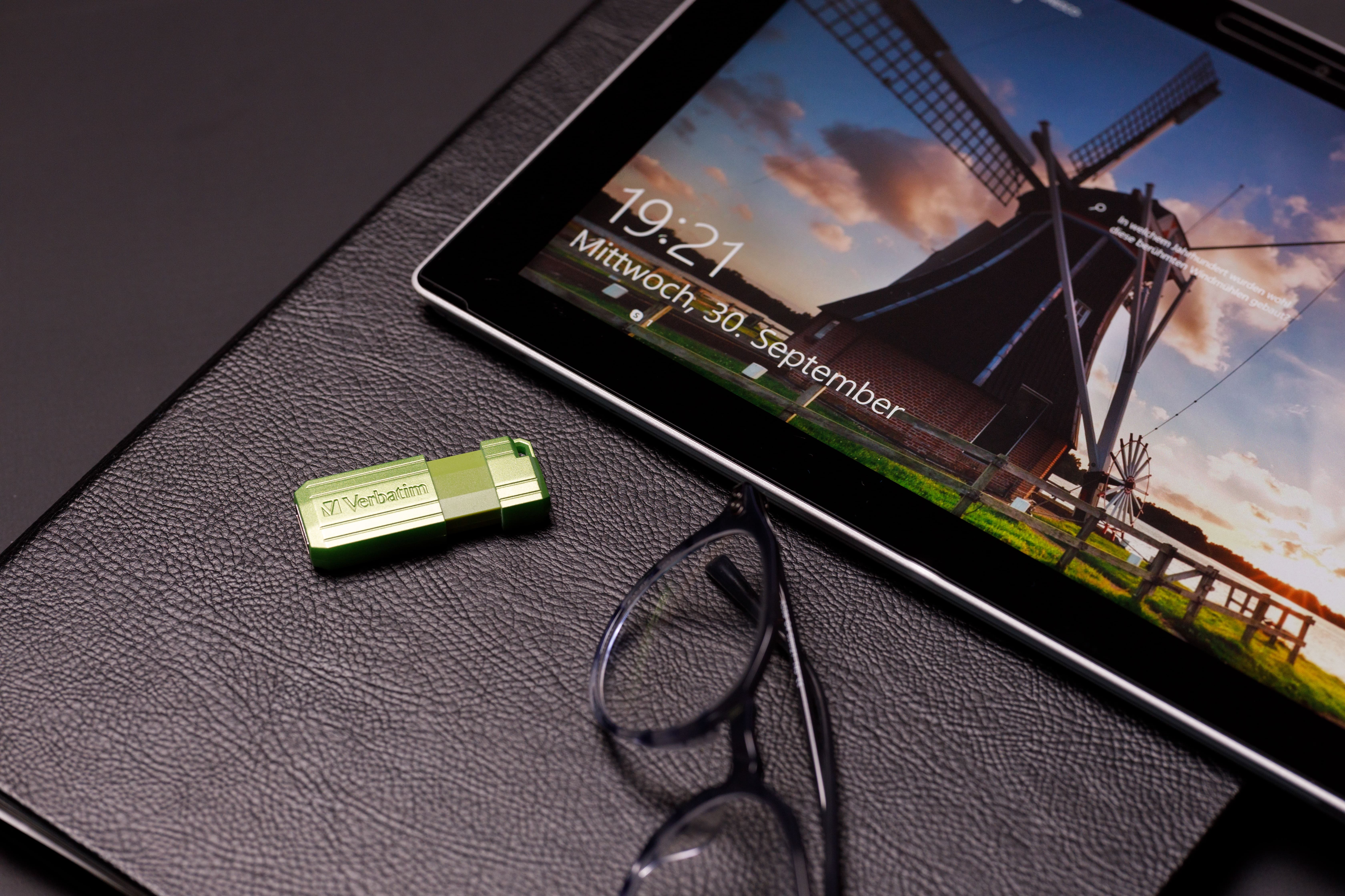 Un tablet con una scena di mulino, con una chiavetta USB, occhiali e una superficie nera.