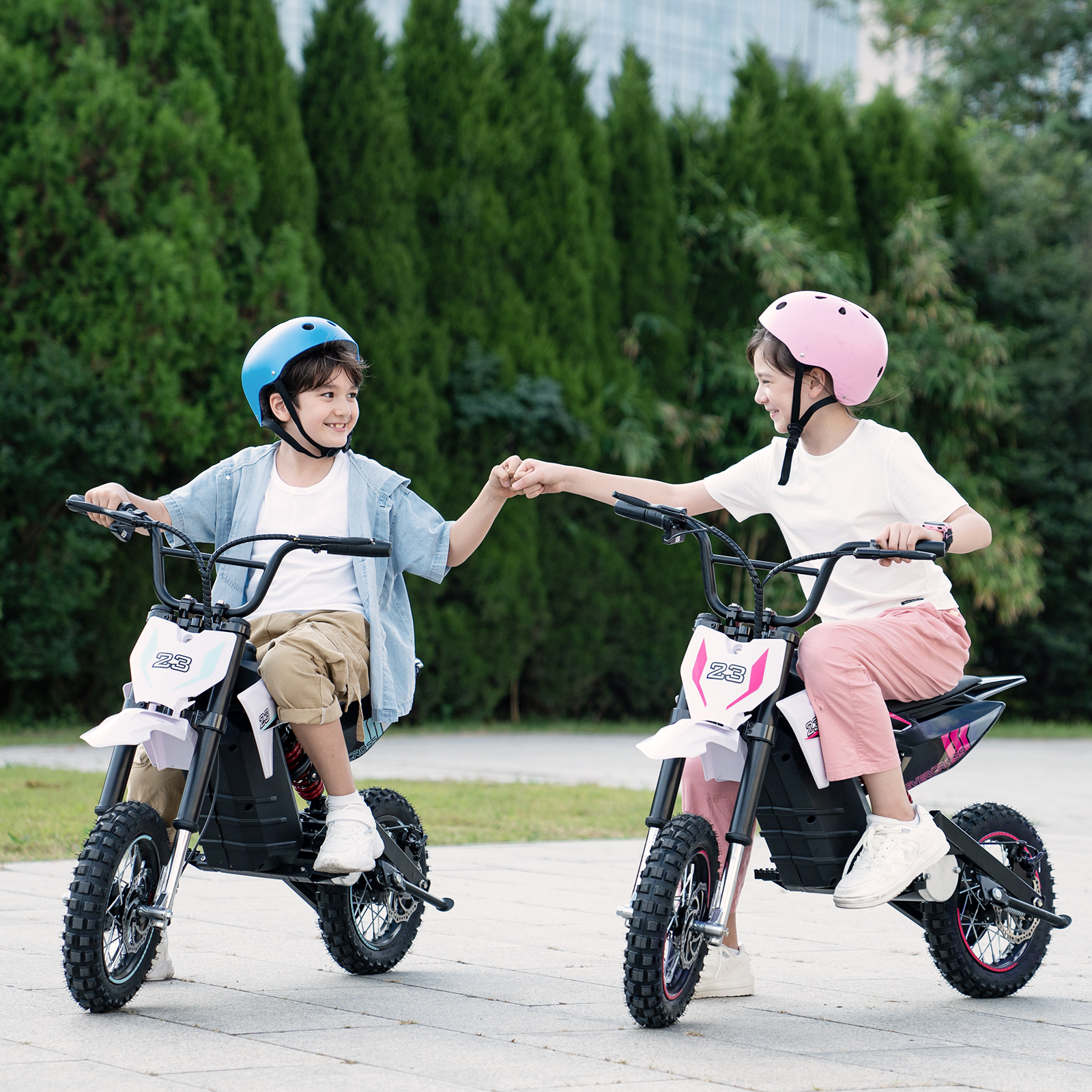Zwei Kinder auf Elektromotorrädern, die Helme tragen, stehen kurz vor dem Faustschlag. Die Fahrräder sind weiß und rosa.
