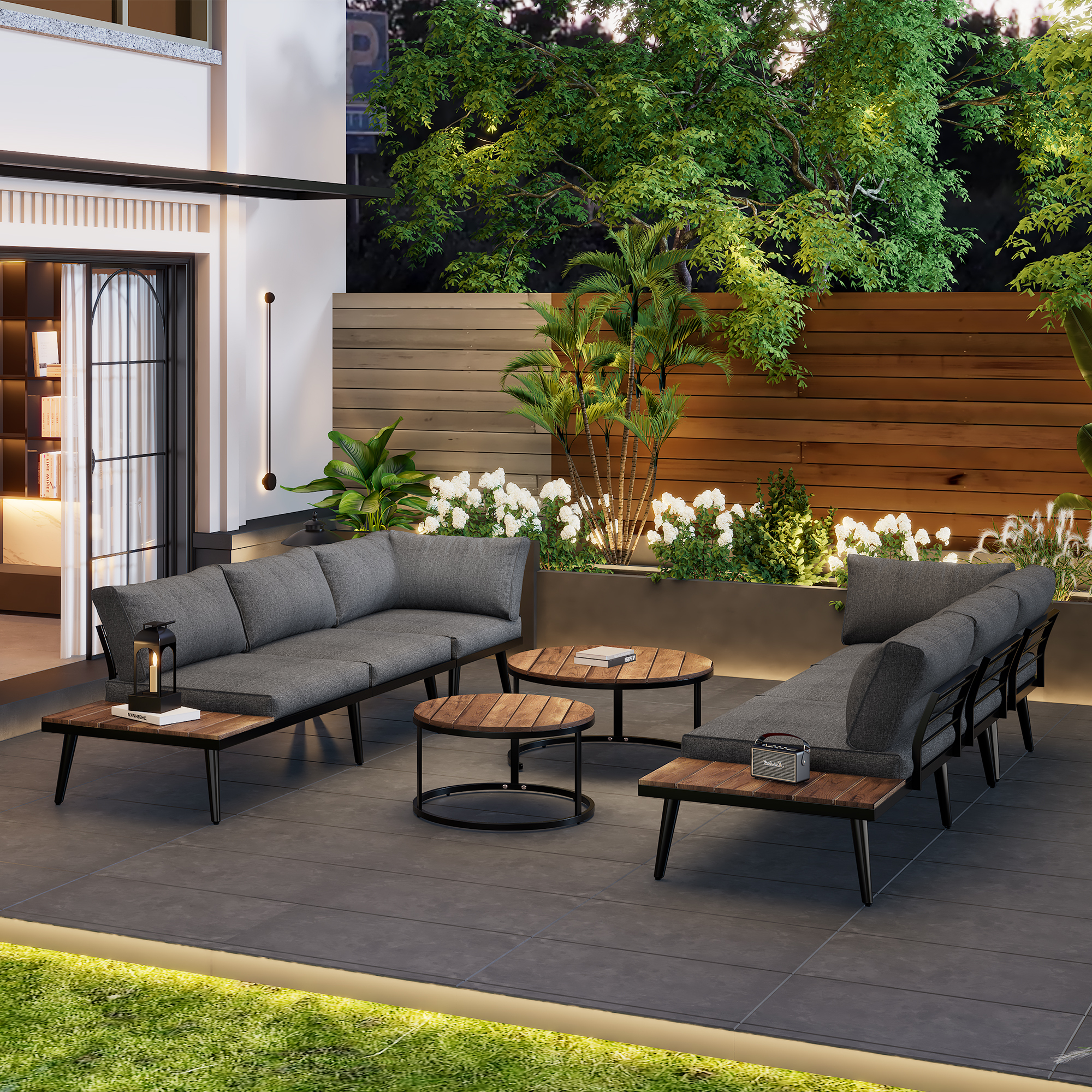Gartenmöbel-Set. Graue Sofas und runde Tische auf einer grauen Terrasse. Grüne Pflanzen im Hintergrund.