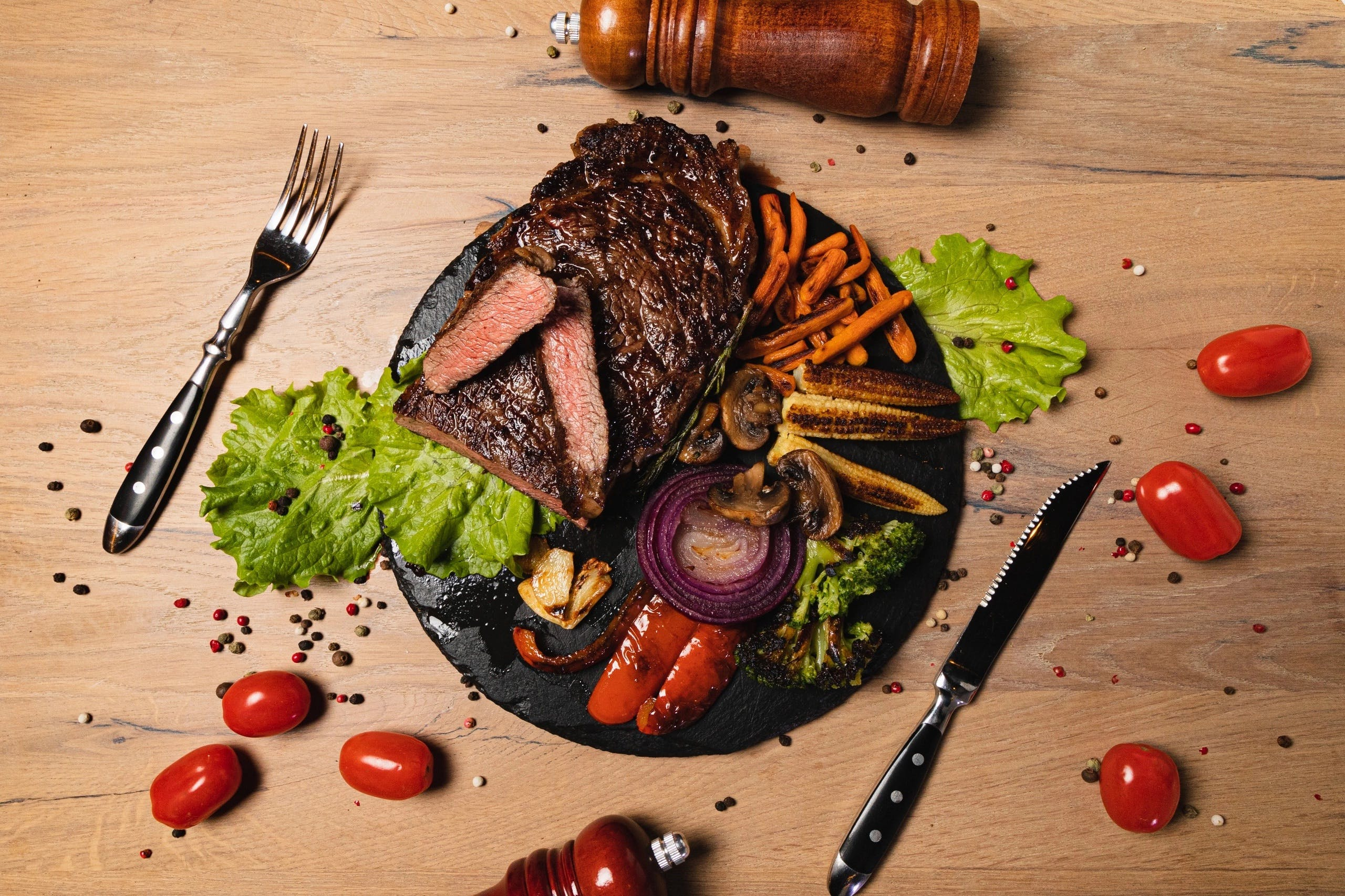 Bovenaanzicht van een bord met steak, groenten en kruiden op een houten tafel.