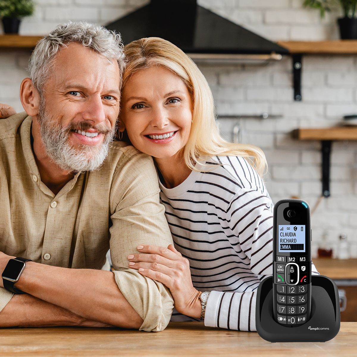 Lachend ouder echtpaar poseert thuis. Een draadloze telefoon staat op tafel. Keuken op de achtergrond.