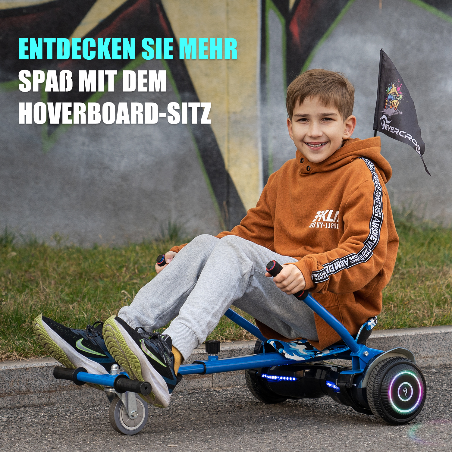 Junge fährt einen Hoverboard-Sitz. Grünes Gras, grauer Bürgersteig und Graffiti-Hintergrund.