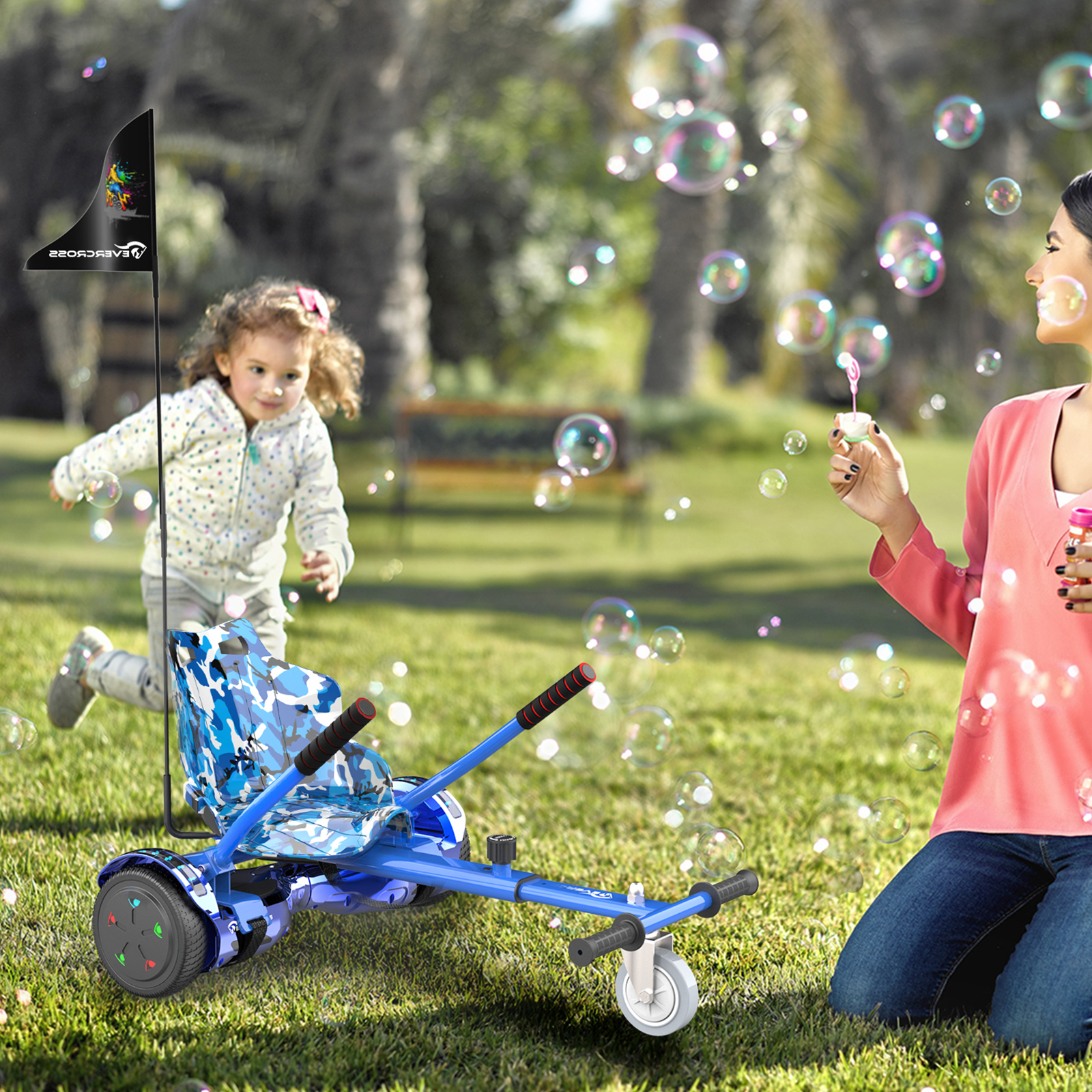 Una bambina corre dietro un go-kart blu mentre una donna fa bolle in un parco.