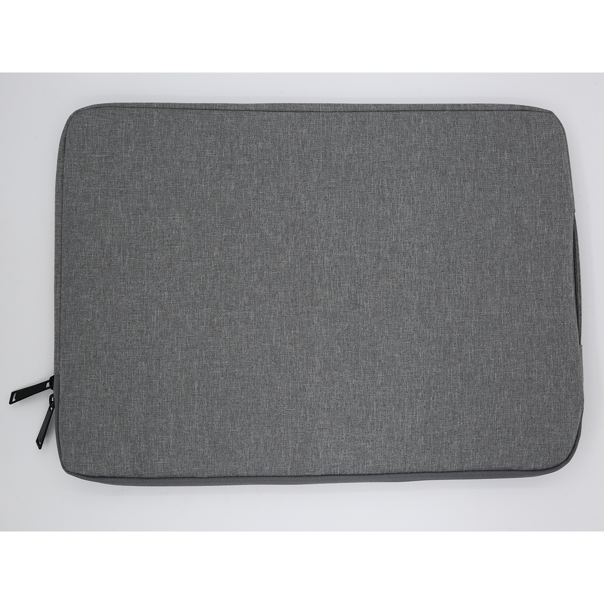 Szara torba na laptopa z zamkiem błyskawicznym po prawej stronie. Torba leży na białej powierzchni.