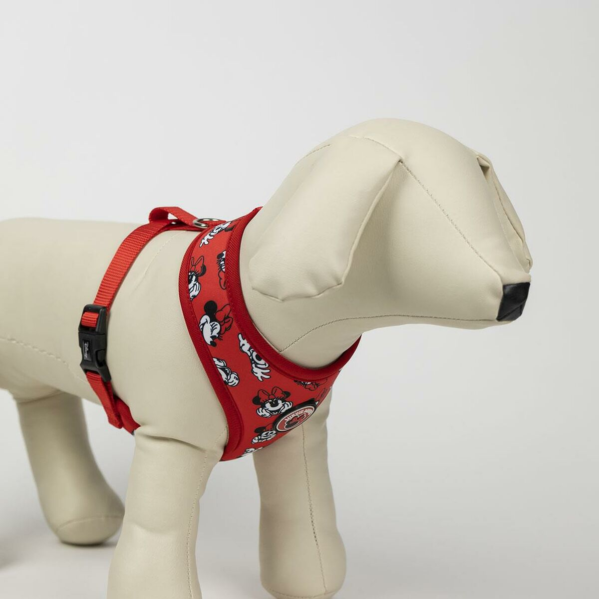 Hund trägt ein rotes Geschirr mit Minnie-Maus-Muster. Das Geschirr befindet sich auf einer weißen Schaufensterpuppe. Weißer Hintergrund.