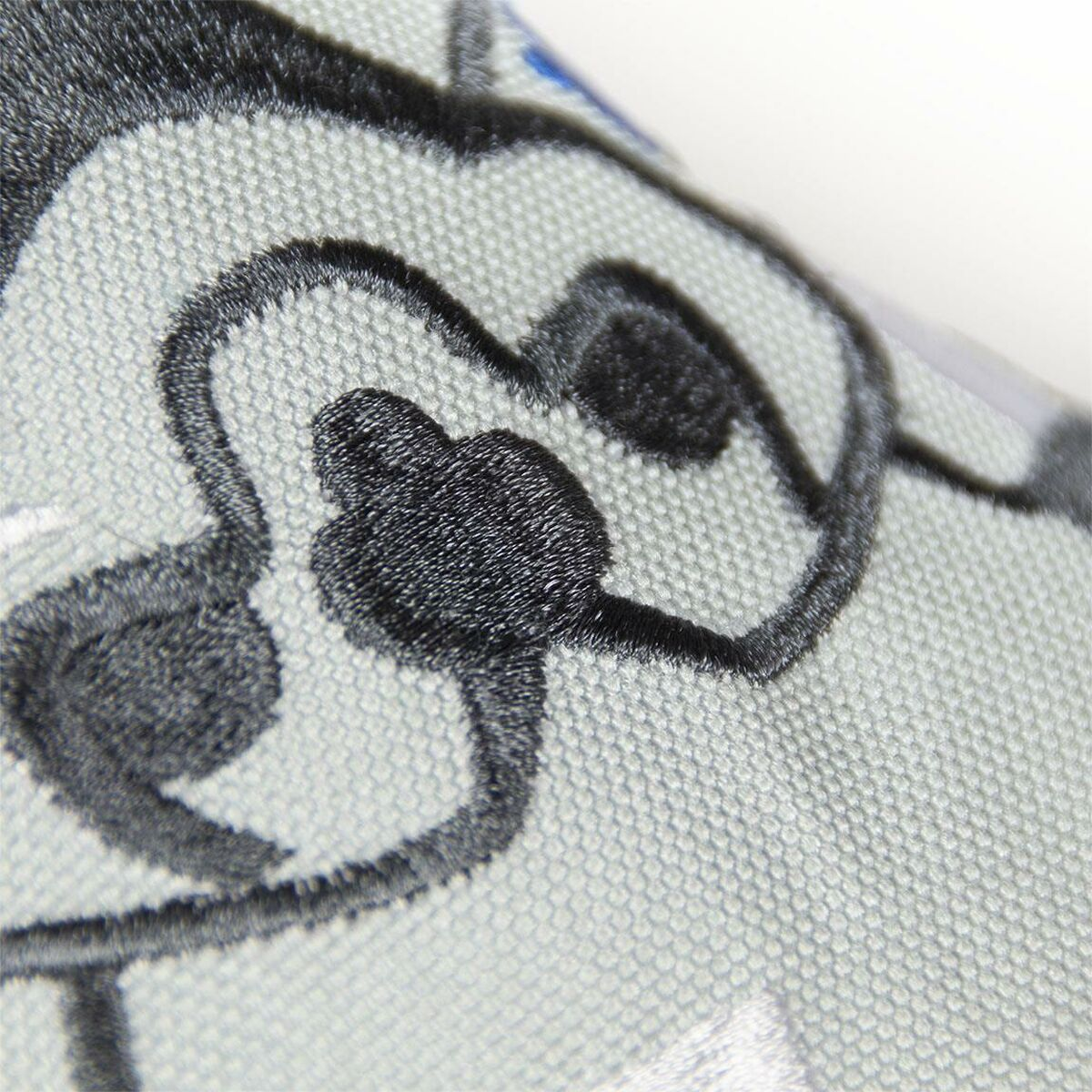 Nahaufnahme von gestickter Cartoonfigur auf grauem Stoff, schwarze Kontur.