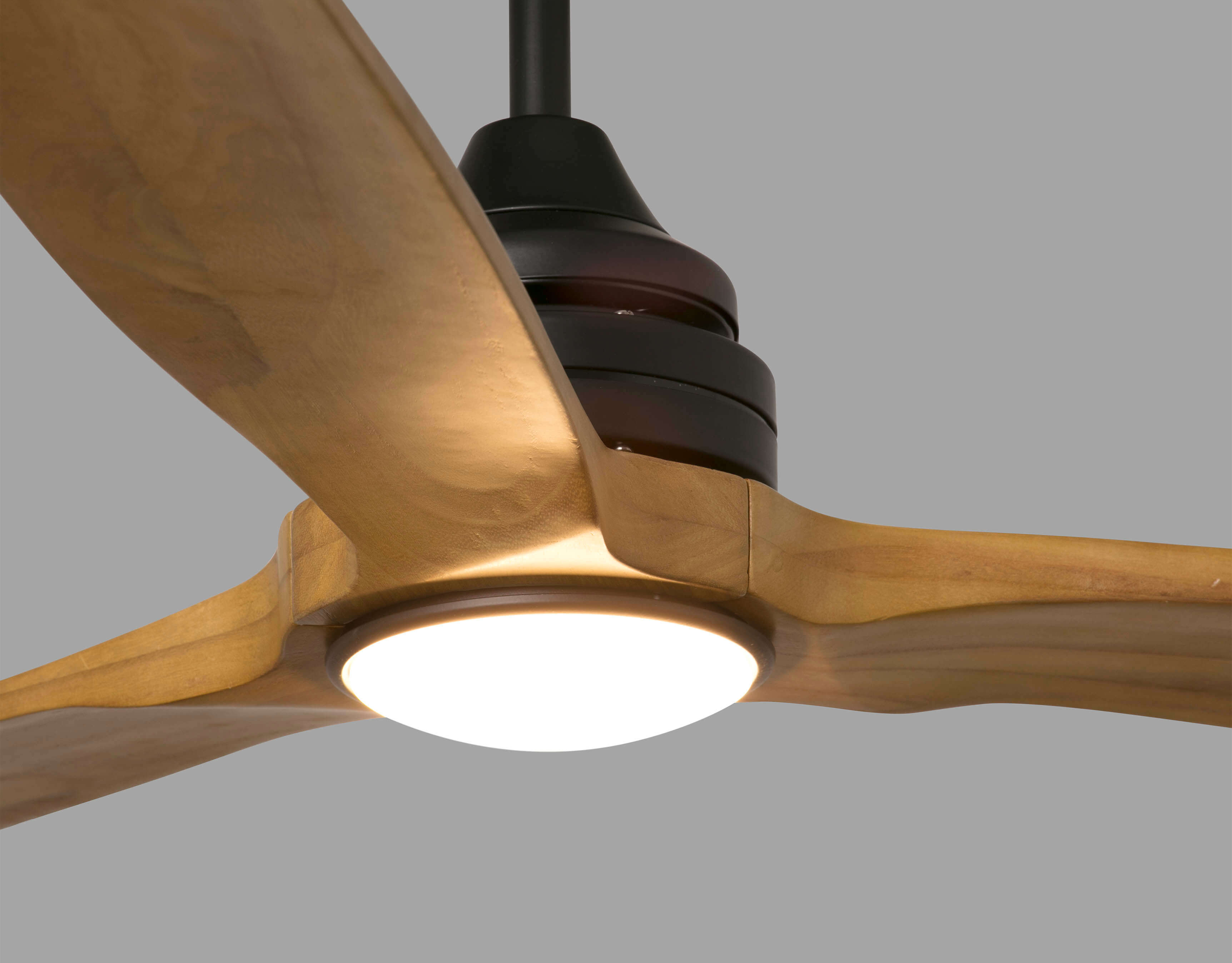 Primo piano di un ventilatore a soffitto con pale in legno e luce centrale. Lo sfondo è grigio chiaro.