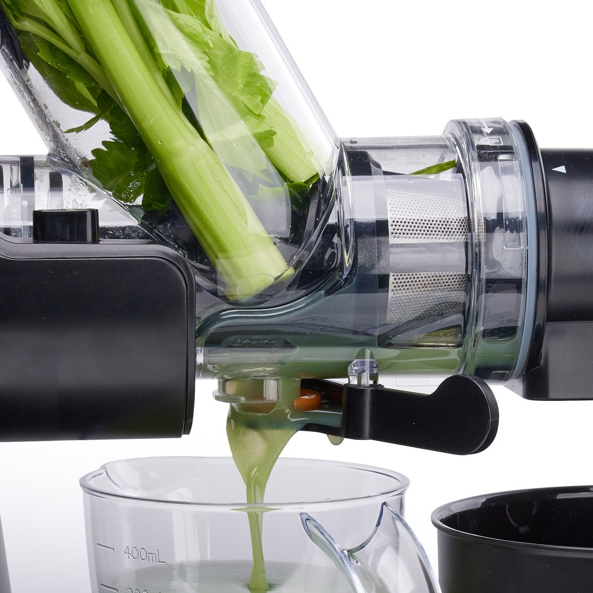 Entsafter mit Sellerie, der entsaftet wird. Grüner Saft fließt in einen Messbecher.