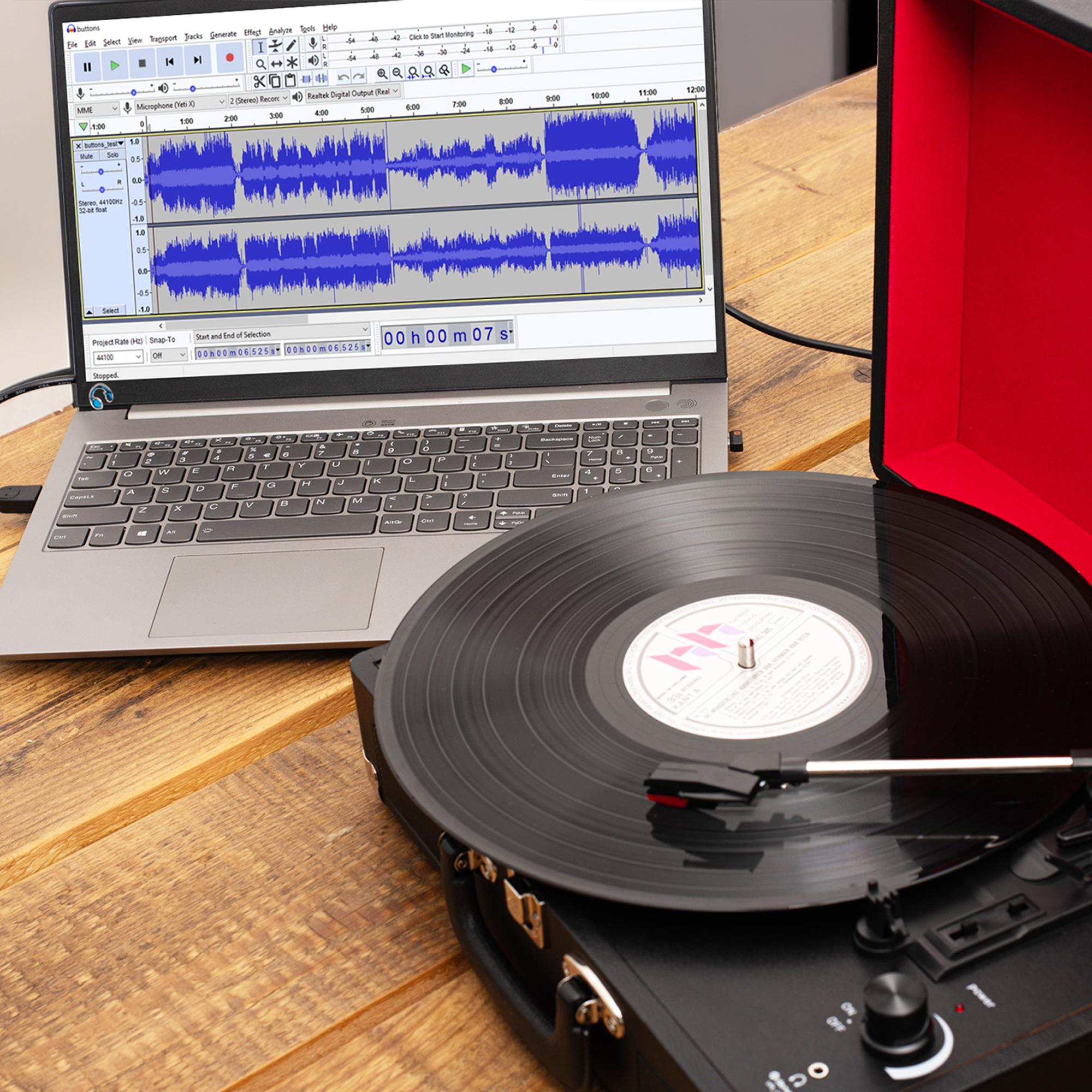 Laptop i gramofon na drewnianym stole. Ekran wyświetla oprogramowanie do edycji audio.