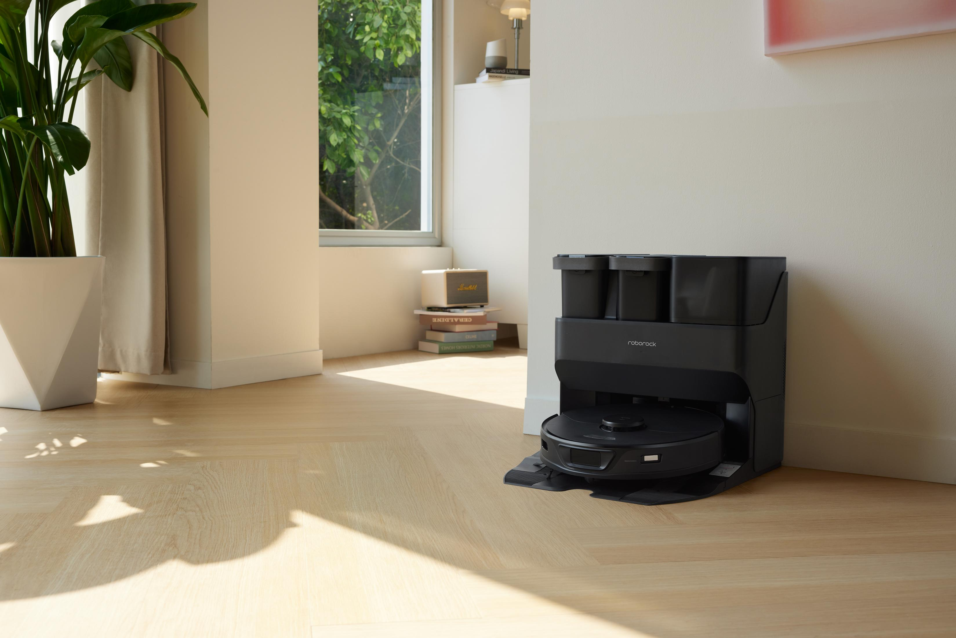Czarny odkurzacz robot w stacji ładującej, w pokoju z drewnianą podłogą.