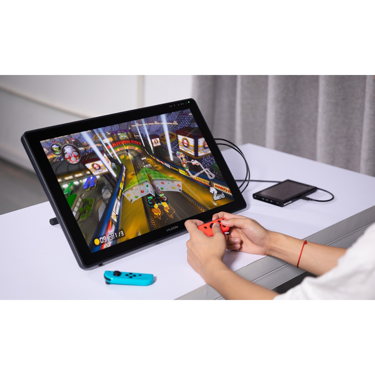 Persona che gioca a un videogioco su un tablet da disegno con gioco visualizzato, tenendo un controller rosso.