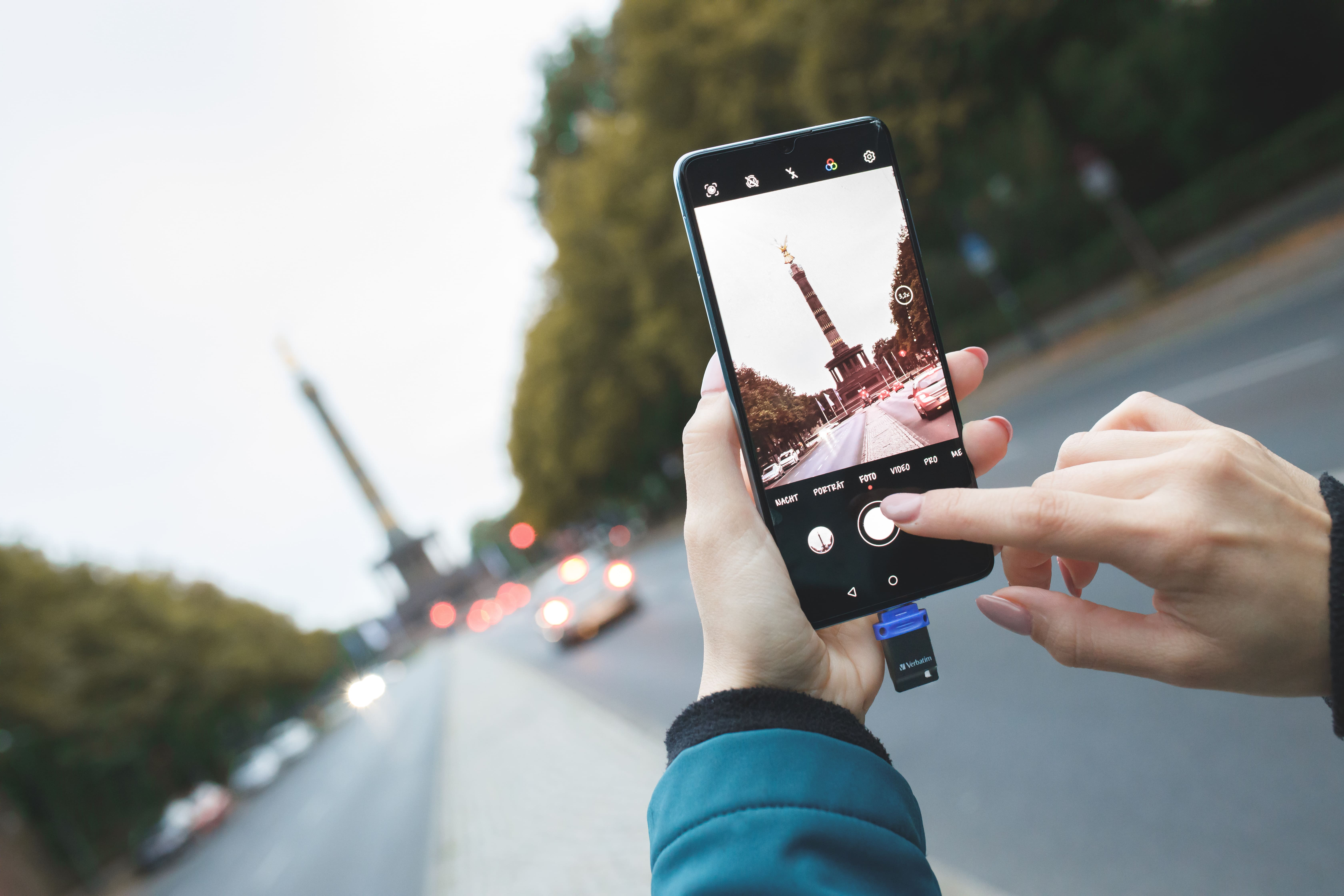 Osoba trzyma smartfon, robiąc zdjęcie berlińskiego pomnika z podłączonym pendrivem.