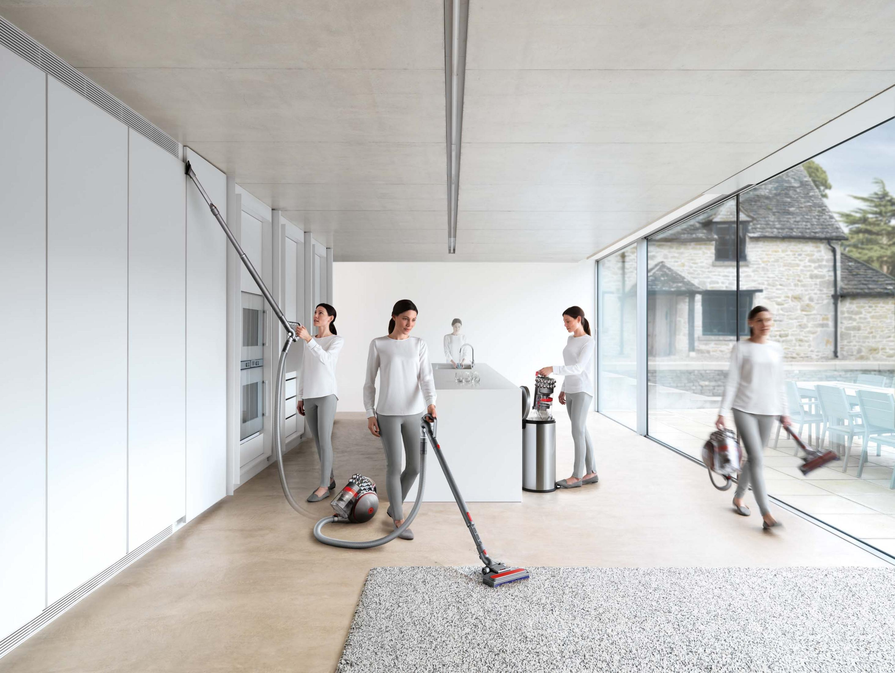 Mehrere Frauen staubsaugen in einem modernen, minimalistischen Zuhause mit weißen Wänden und einem großen Fenster.