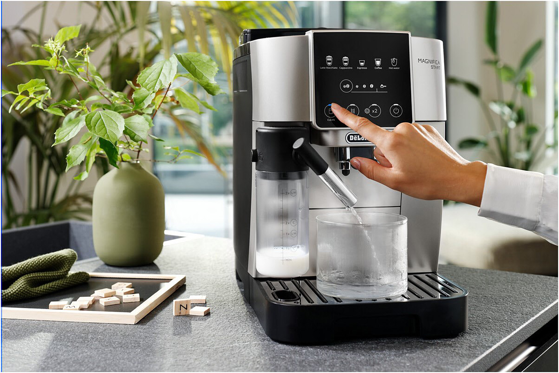 Person operating espresso machine with a glass of water and a plant.