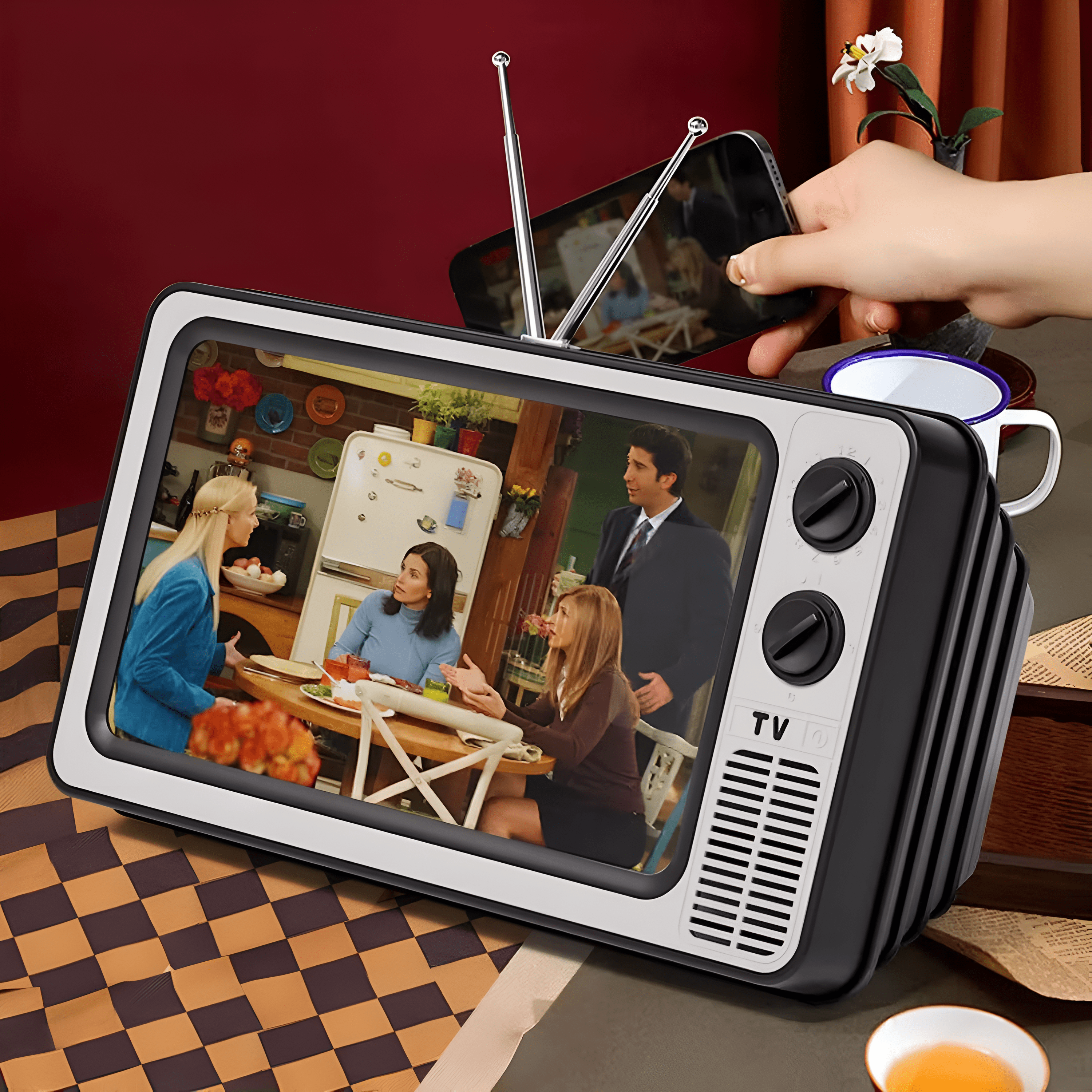 Televisor retro con una escena de Friends. Una mano sostiene un teléfono con una pantalla que muestra la TV.