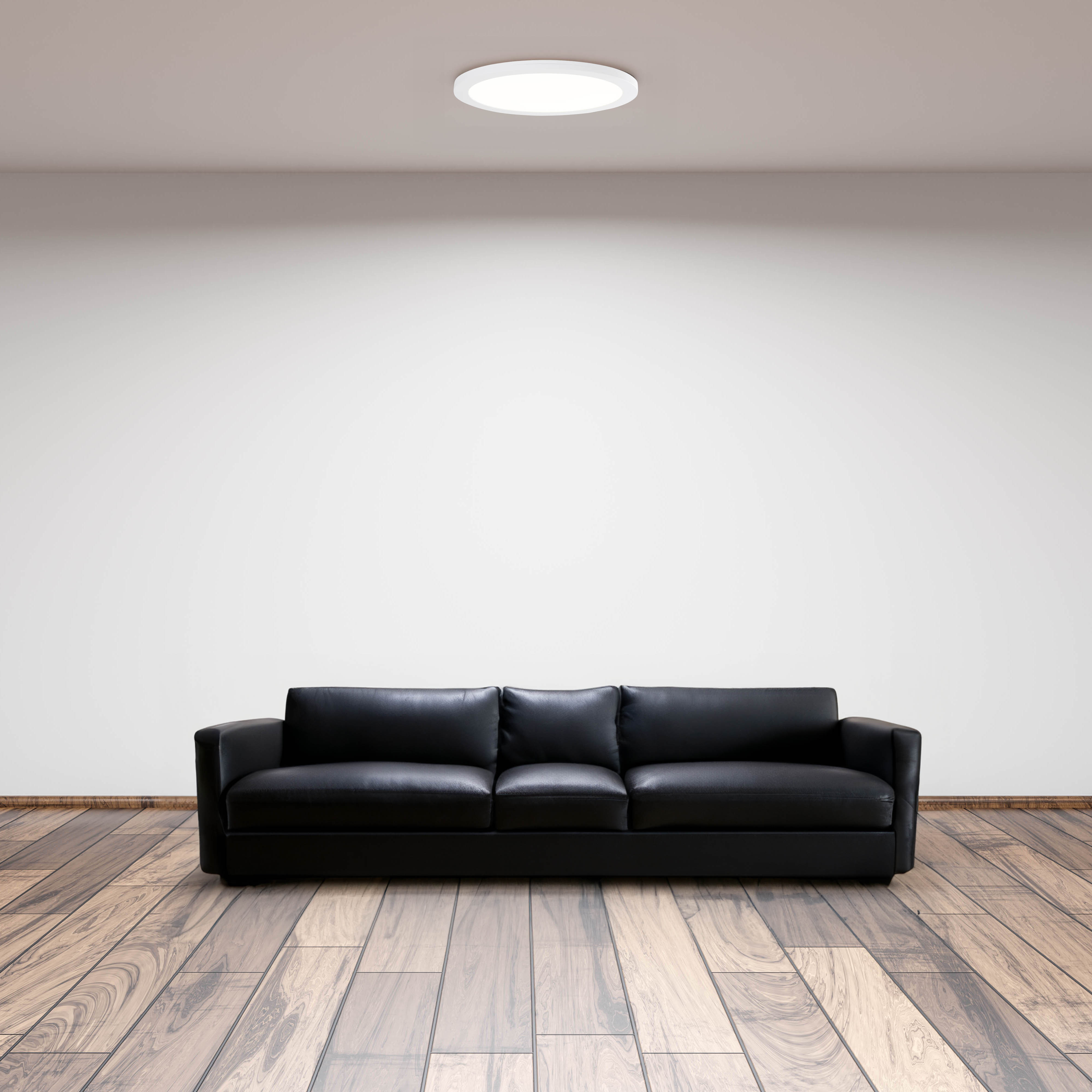 Ein schwarzes Ledersofa steht auf einem Holzboden vor einer weißen Wand.
