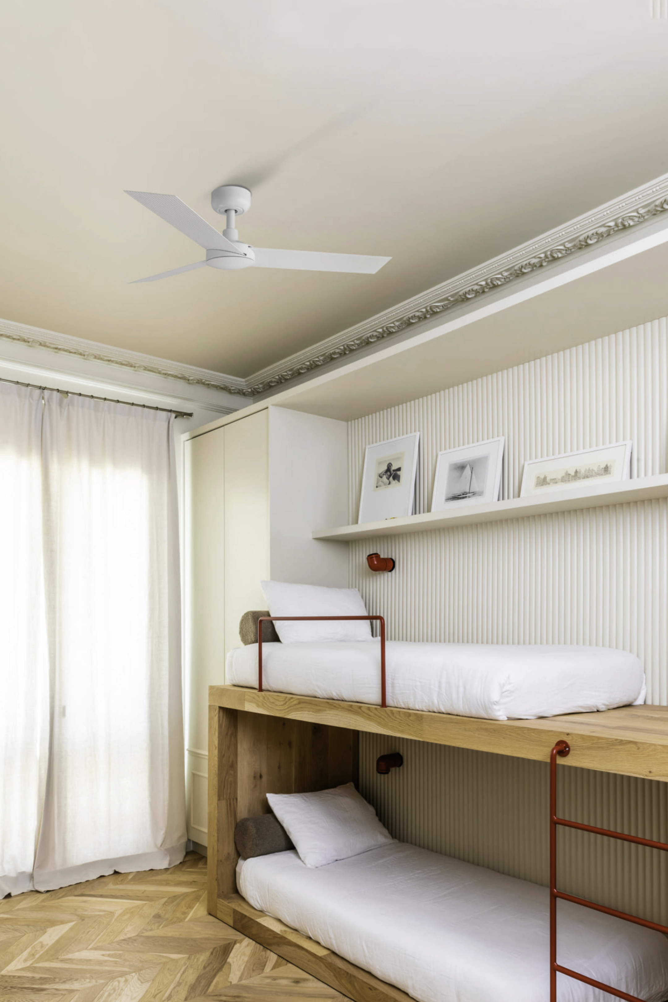 Schlafzimmer-Interieur mit Etagenbetten. Weiße Wände und Decke, Holzböden. Deckenventilator und Kunst an der Wand.