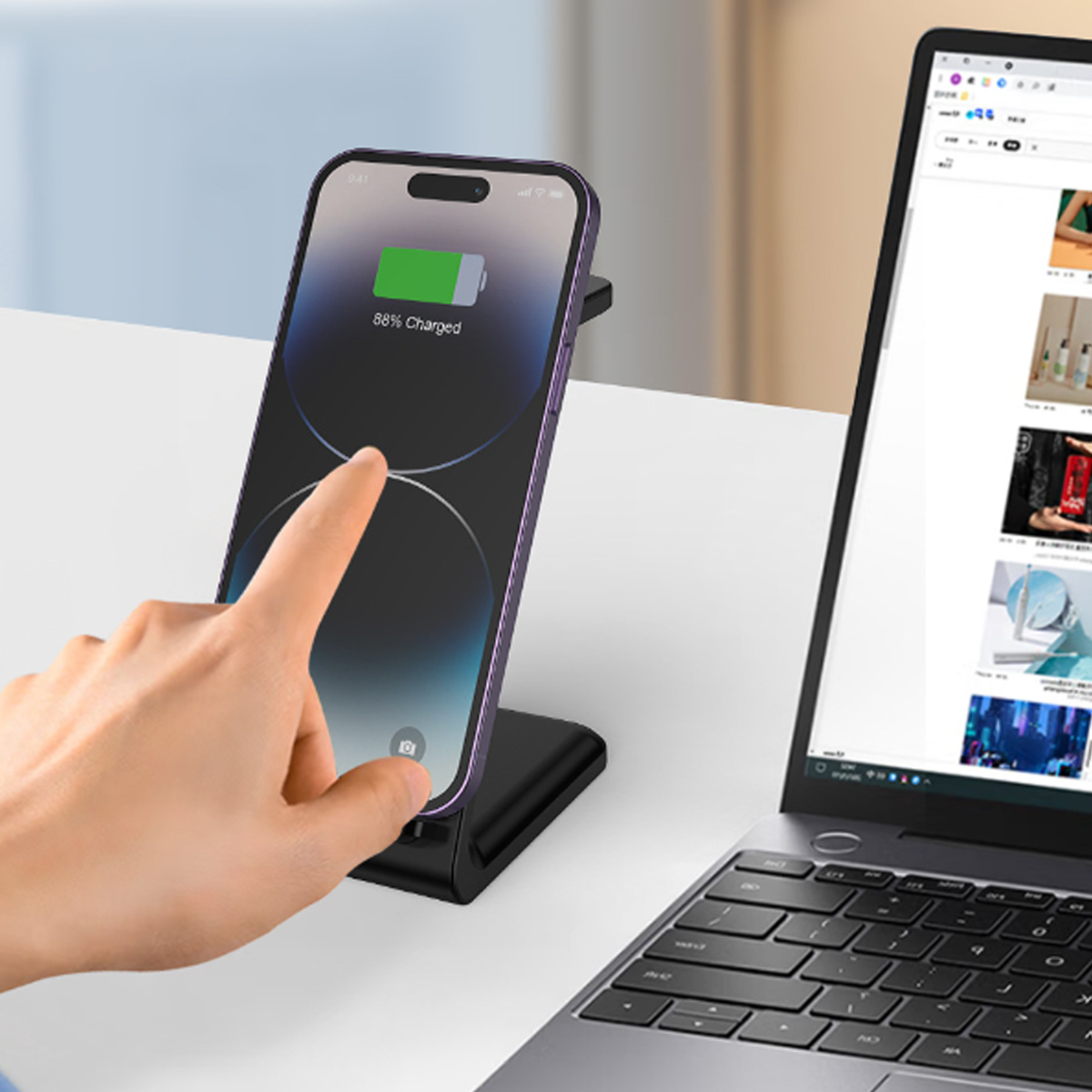 Eine Hand berührt ein Smartphone auf einem kabellosen Ladegerät neben einem Laptop, der eine Website zeigt.