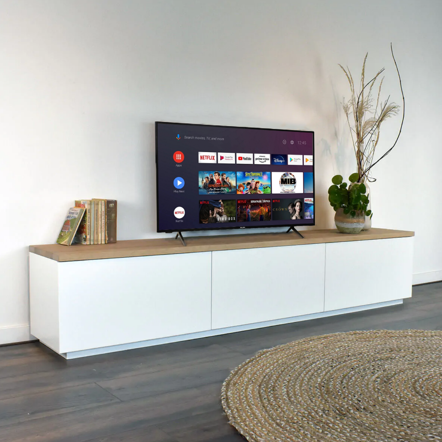 Woonkamer met wit tv-meubel, tv toont apps, planten en een beige vloerkleed.