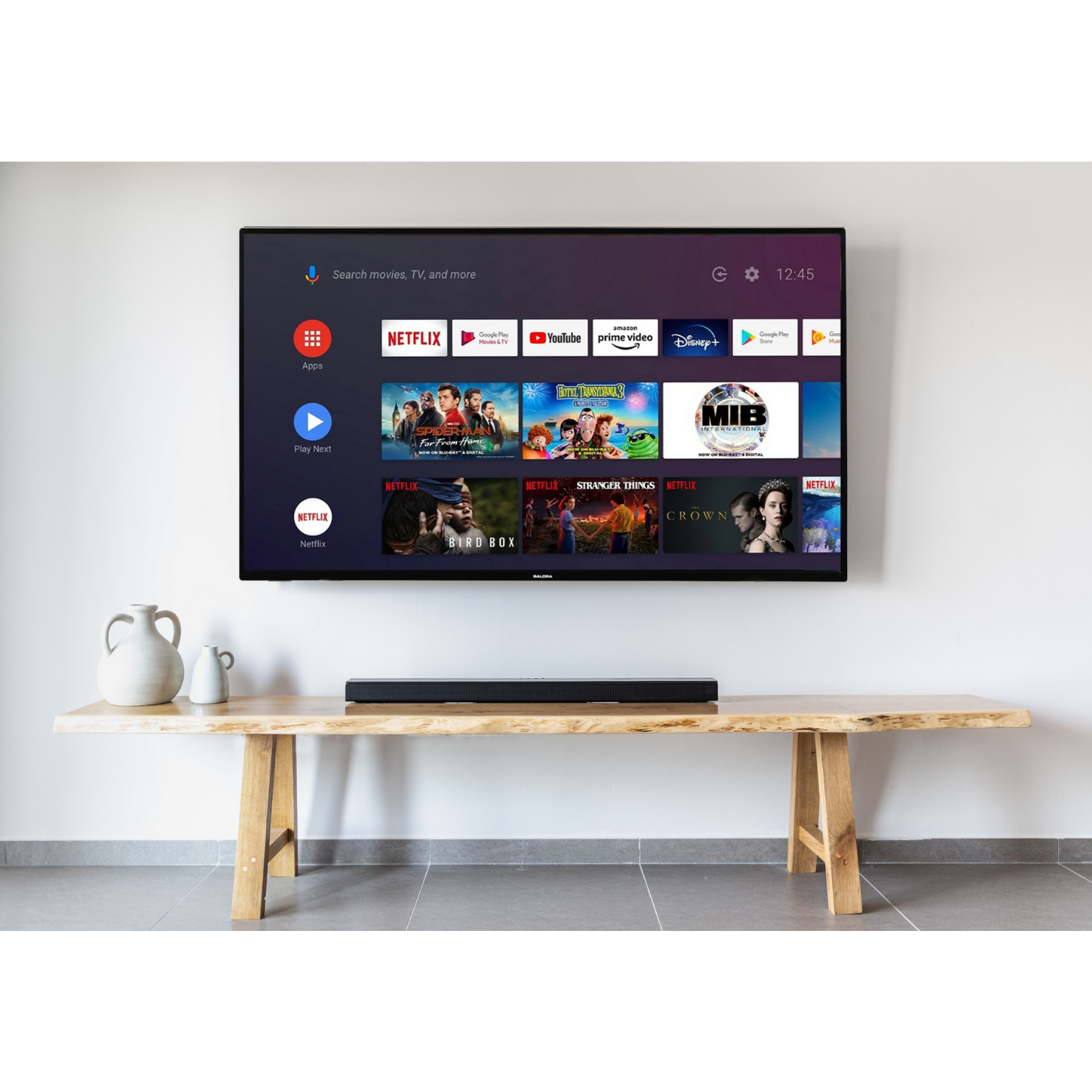 Een tv toont apps. Een soundbar staat onder de tv op een houten tafel. Een witte muur op de achtergrond.