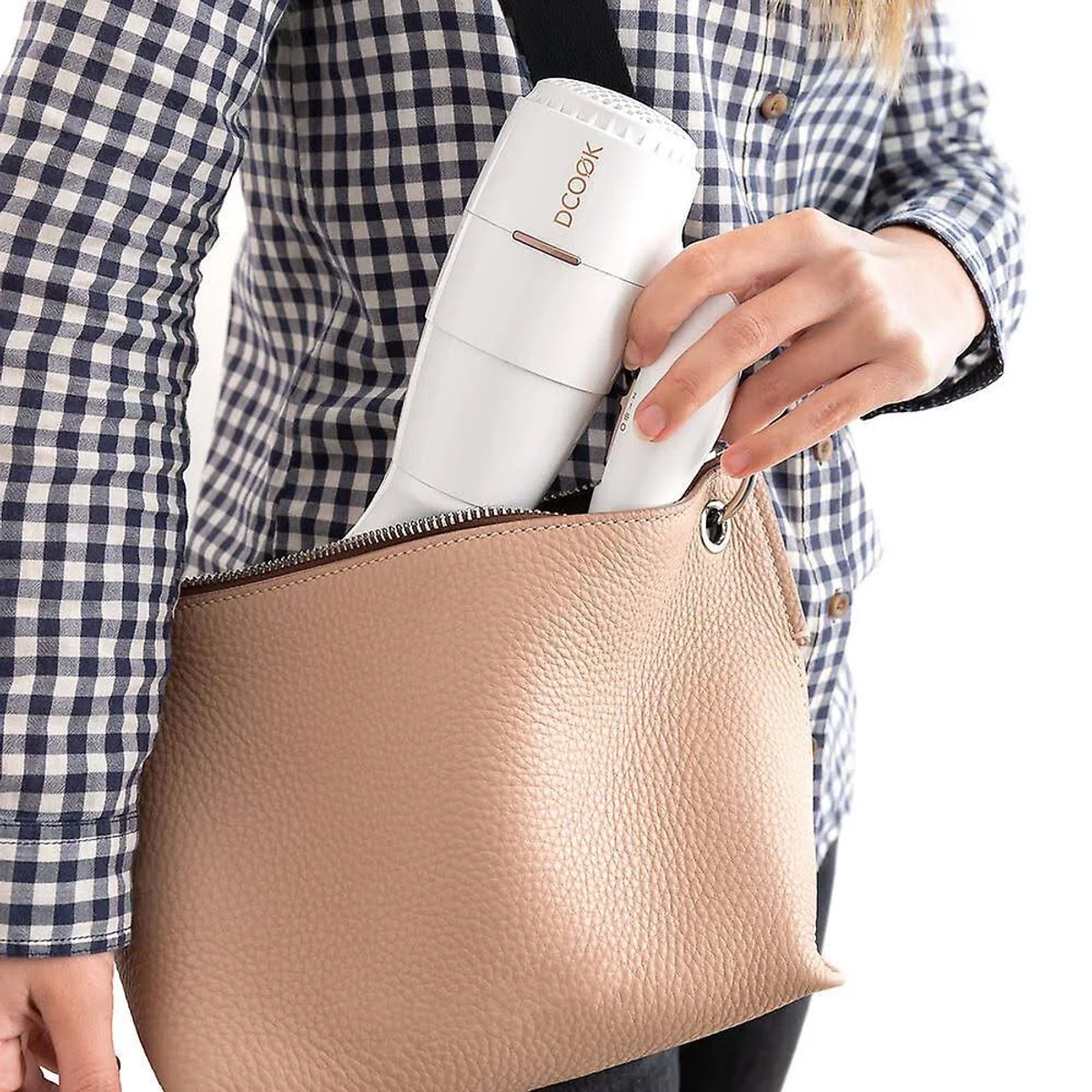 Persona che tiene un asciugacapelli bianco, dentro una borsa beige. Camicia a scacchi. Sfondo bianco.