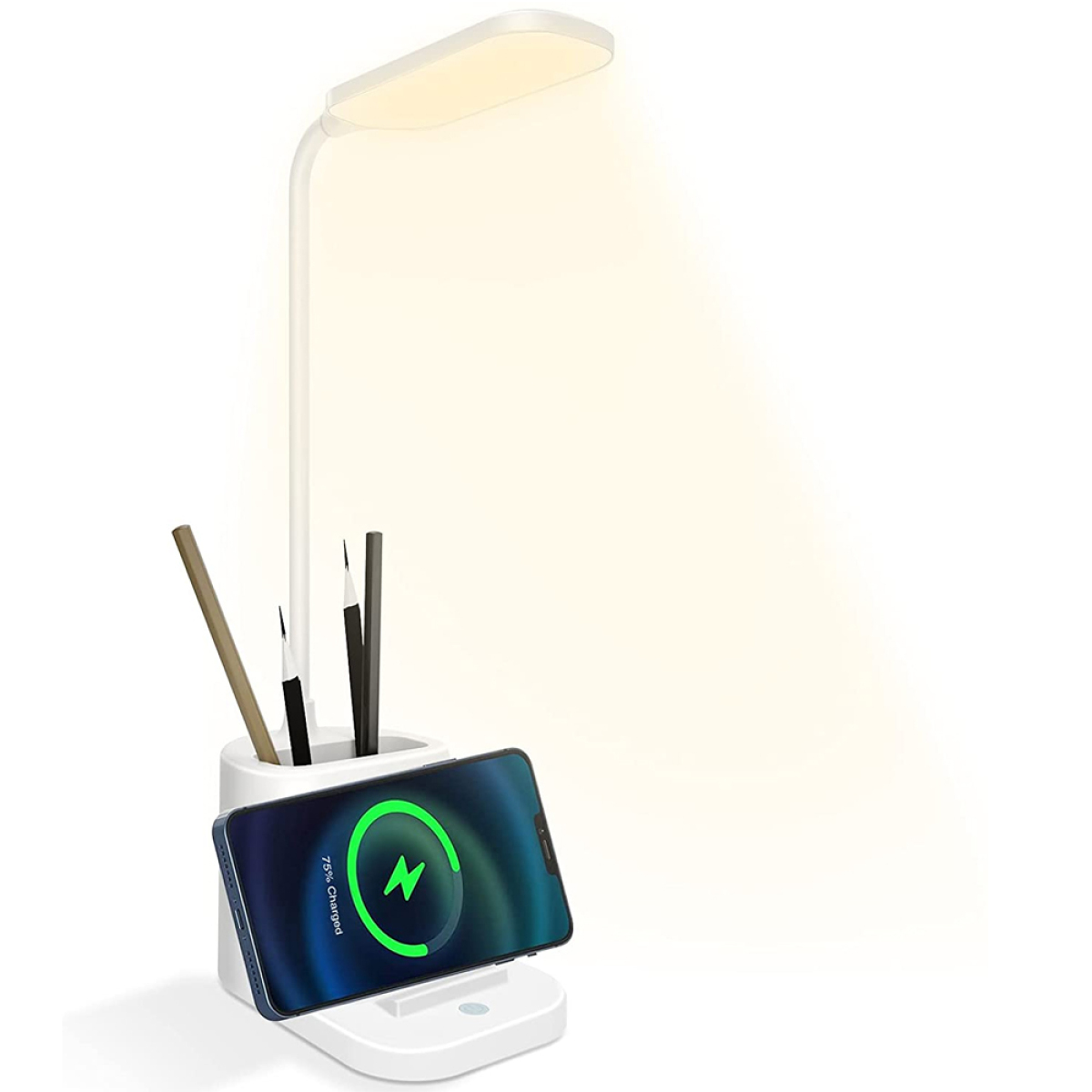 Eine weiße Schreibtischlampe mit einem Telefon, das auf der Basis geladen wird. Bleistifte in einem Halter. Das Licht ist an.