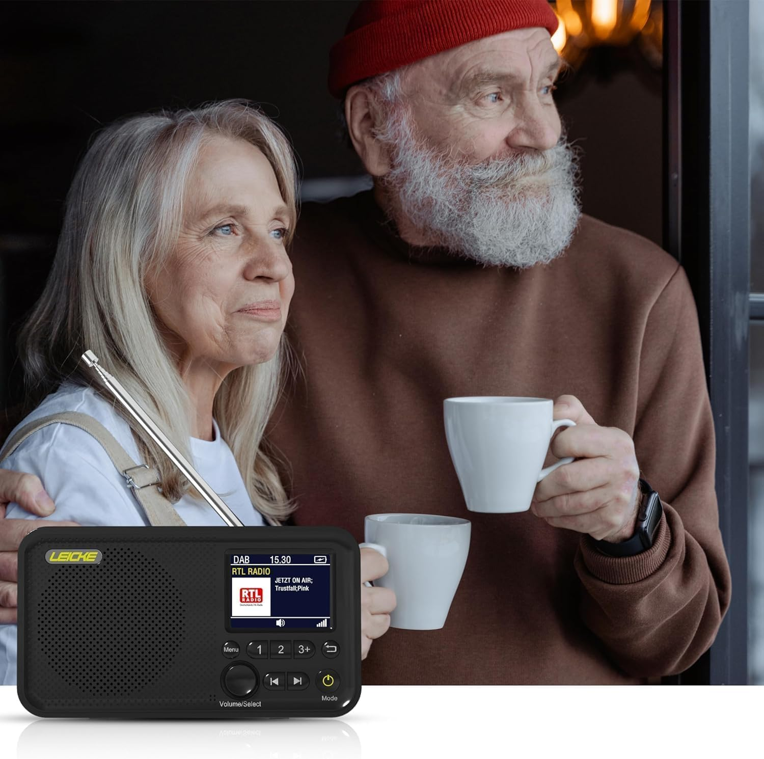 Älteres Ehepaar schaut aus dem Fenster. Mann mit Bart hält eine Tasse. Schwarzes Radio, weiße Tassen.