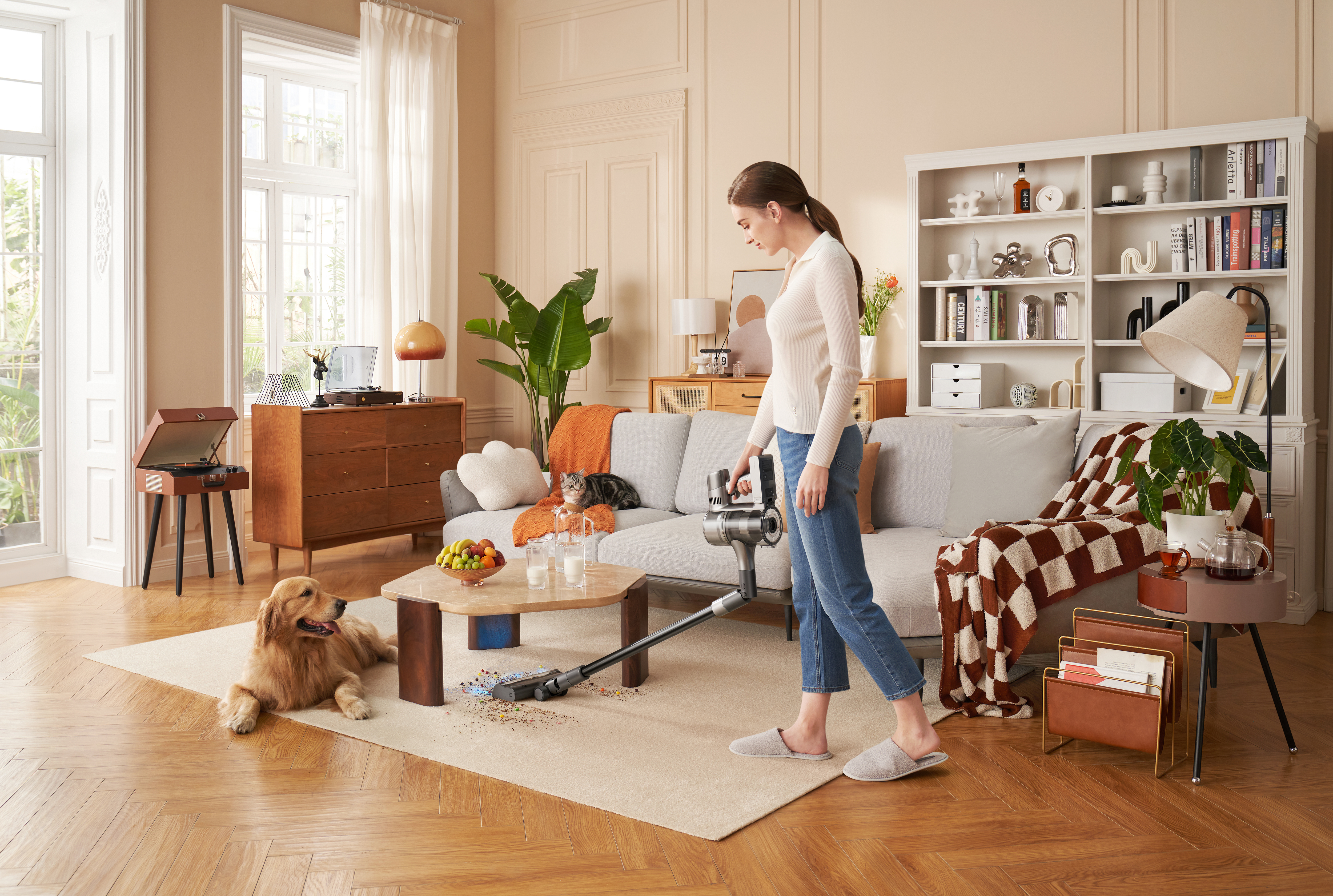 Eine Frau saugt einen Teppichboden im Wohnzimmer, mit Hund, Katze und Möbeln im Hintergrund.