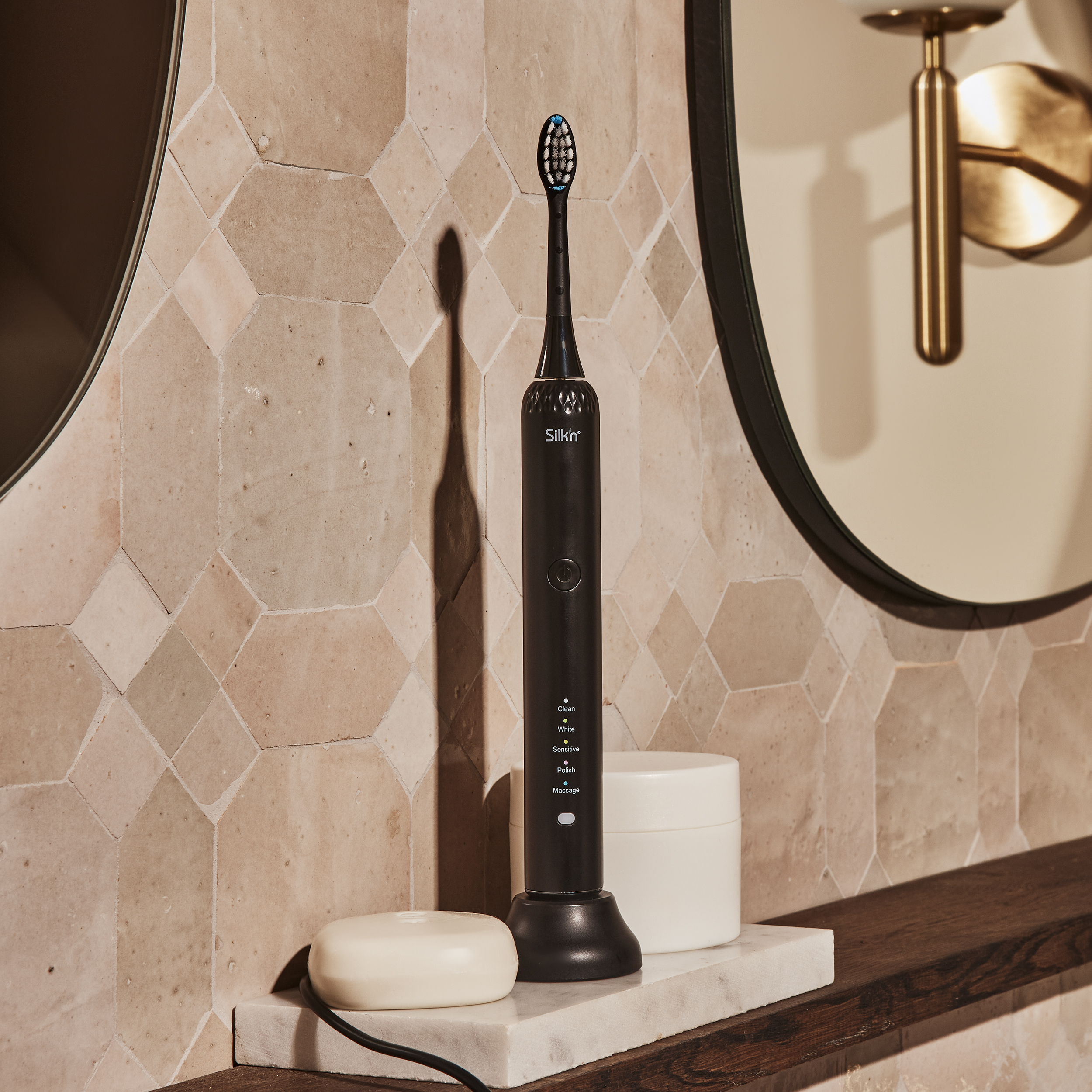 Czarna elektryczna szczoteczka do zębów na stacji ładującej. Na marmurowej półce, z mydłem i lustrem.