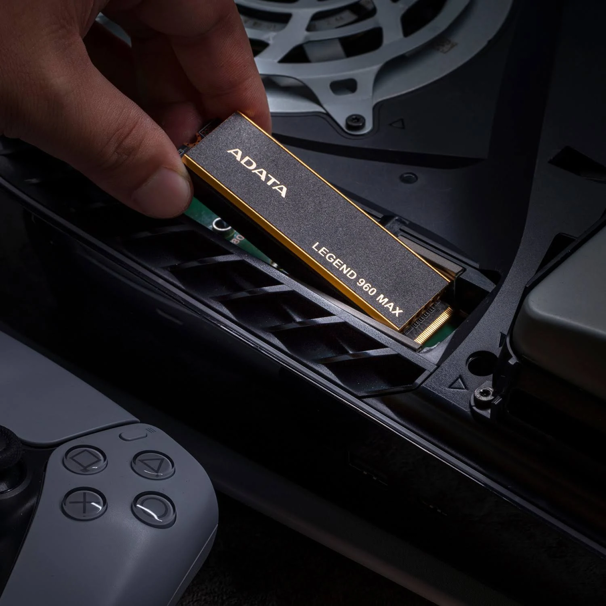 Ręka instalująca dysk SSD ADATA Legend 960 MAX w konsoli, z szarym kontrolerem.