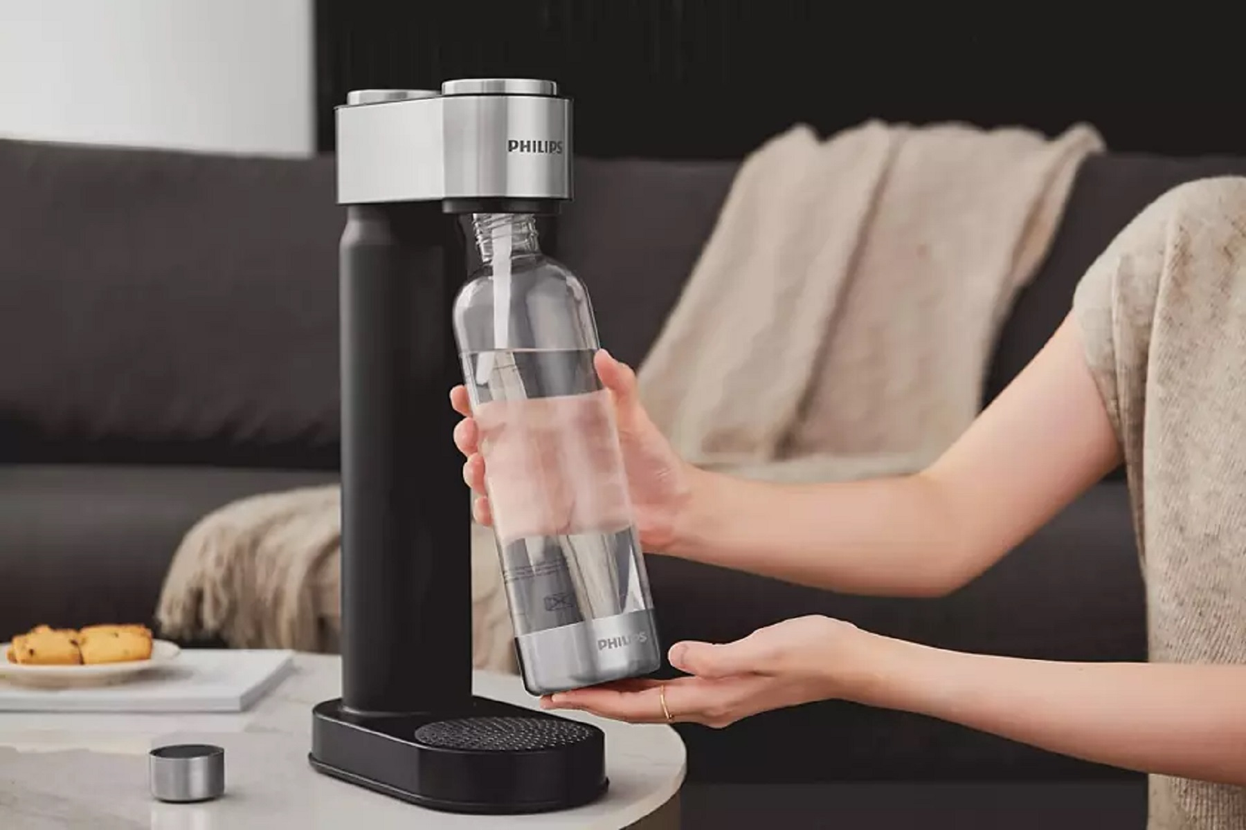 Eine Person hält eine Wasserflasche. Eine Soda-Maschine ist im Hintergrund.