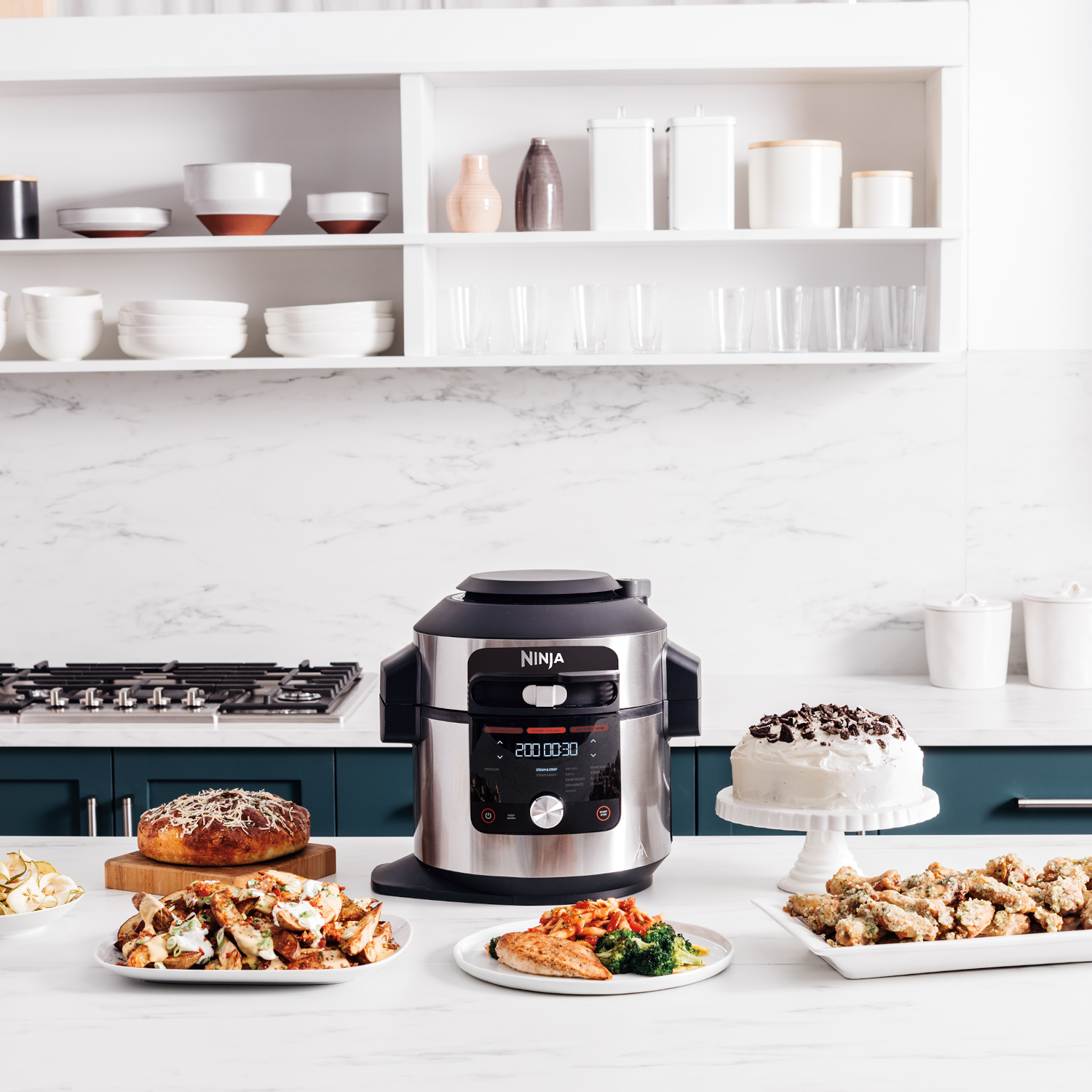 Een keuken met een Ninja foodi, een taart en borden met eten op een wit aanrecht.