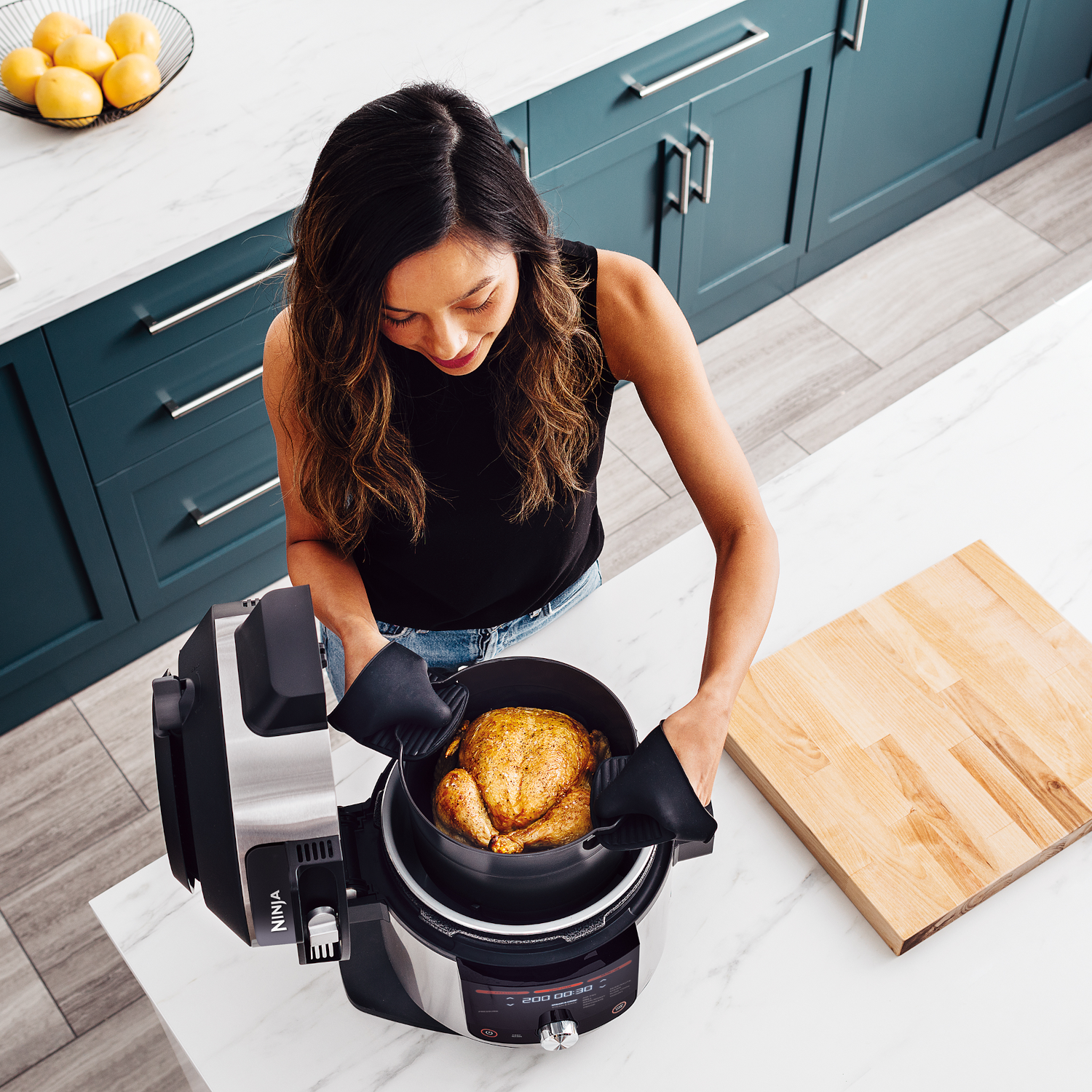Vrouw met zwarte handschoenen die een gekookte kip in een Ninja-kooktoestel plaatst.