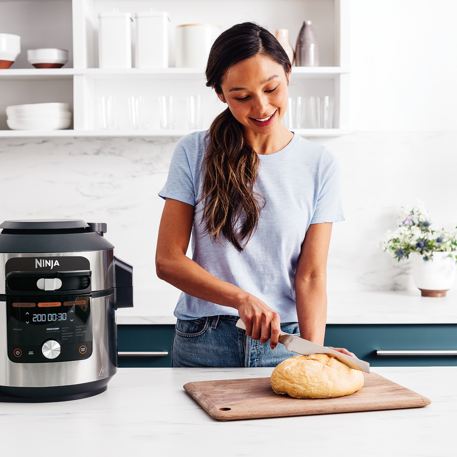 Vrouw snijdt brood in keuken met mes naast een airfryer.
