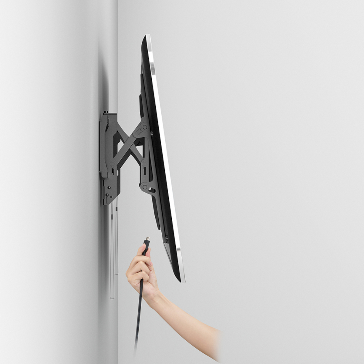 Wandhalterung für Fernseher mit montiertem Fernseher. Eine Hand greift nach einem Kabel.