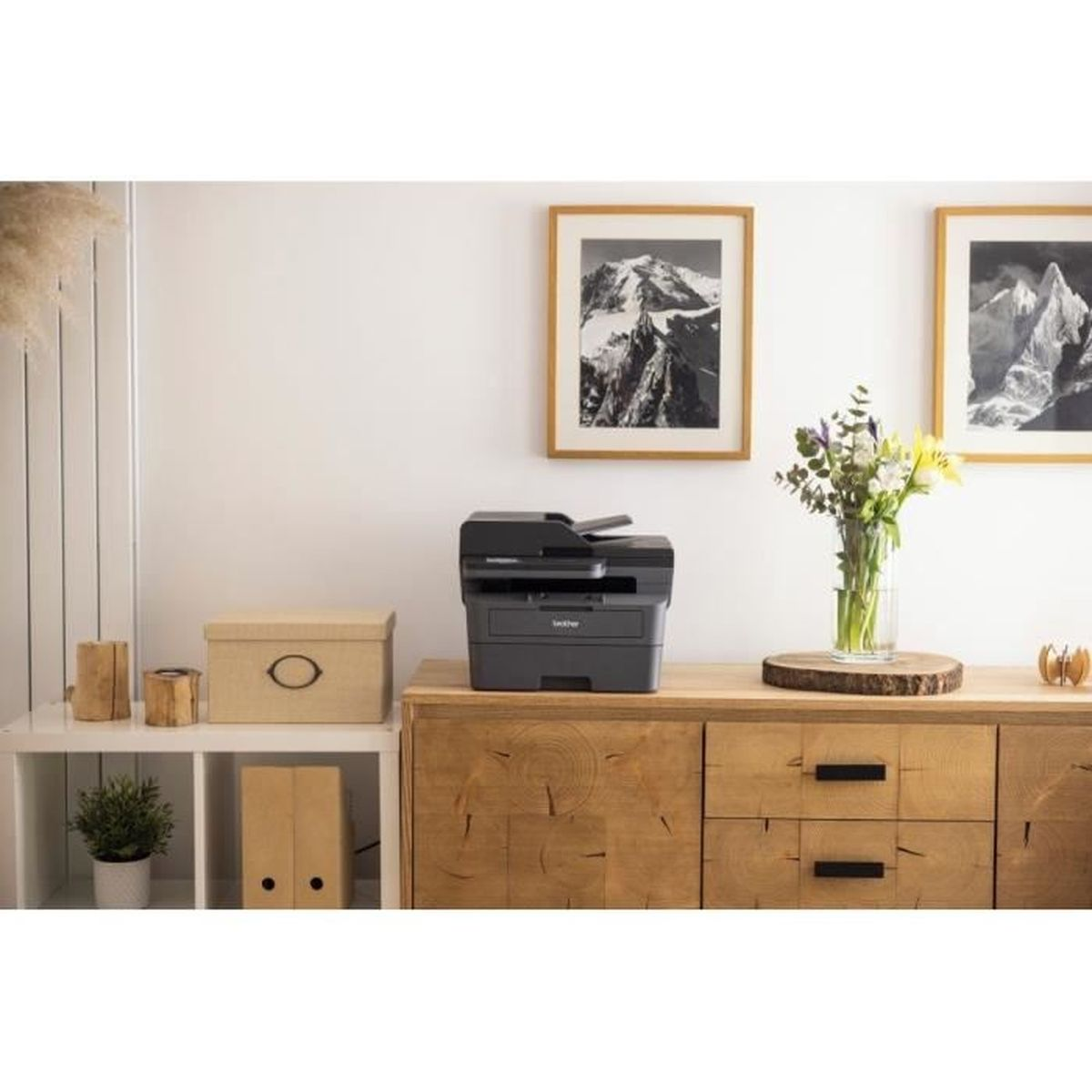 Drukarka na drewnianej szafce, z wazonem kwiatów i oprawioną sztuką górską.