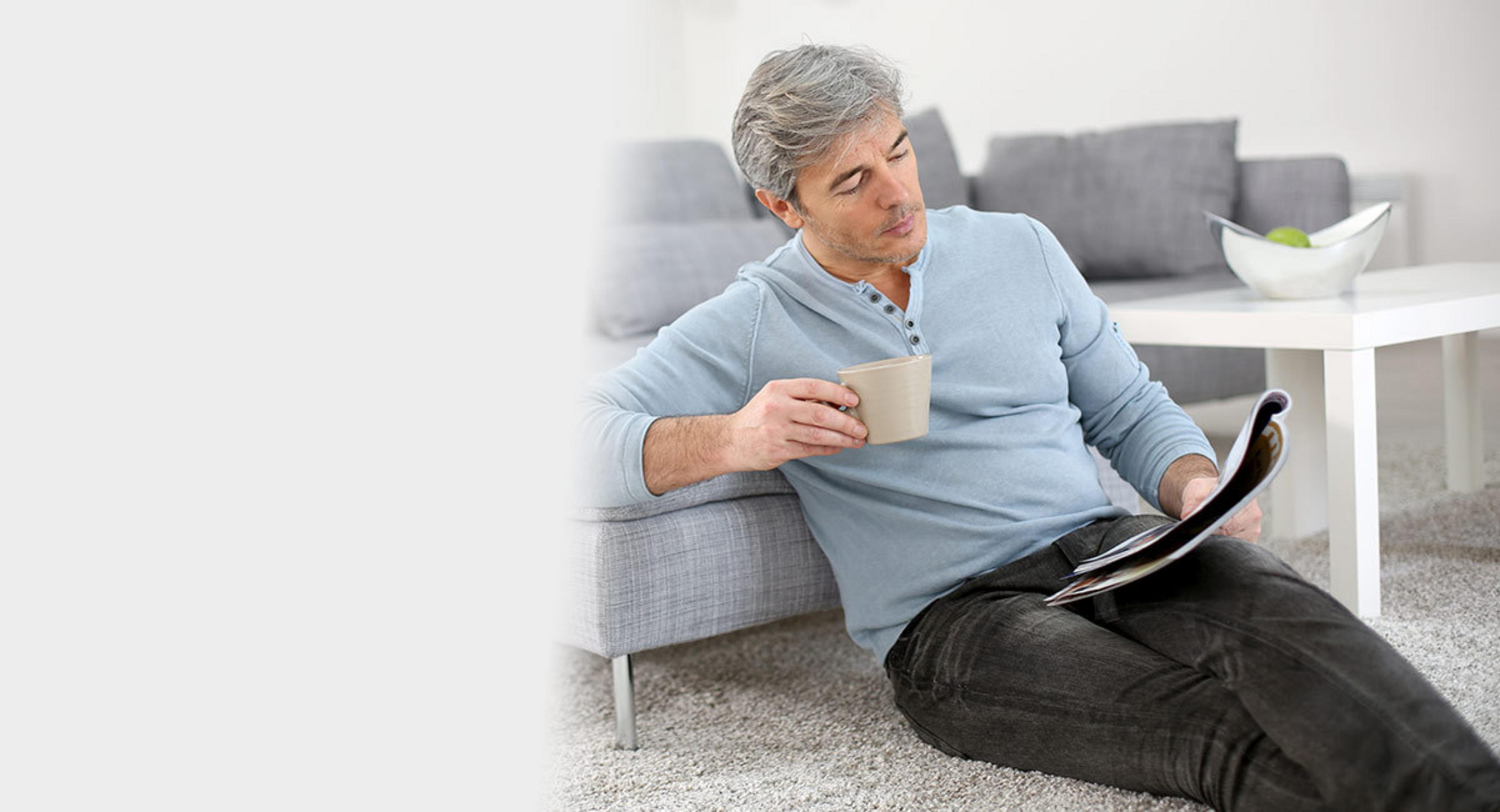 Hombre sentado en el suelo, leyendo una revista, sosteniendo una taza.