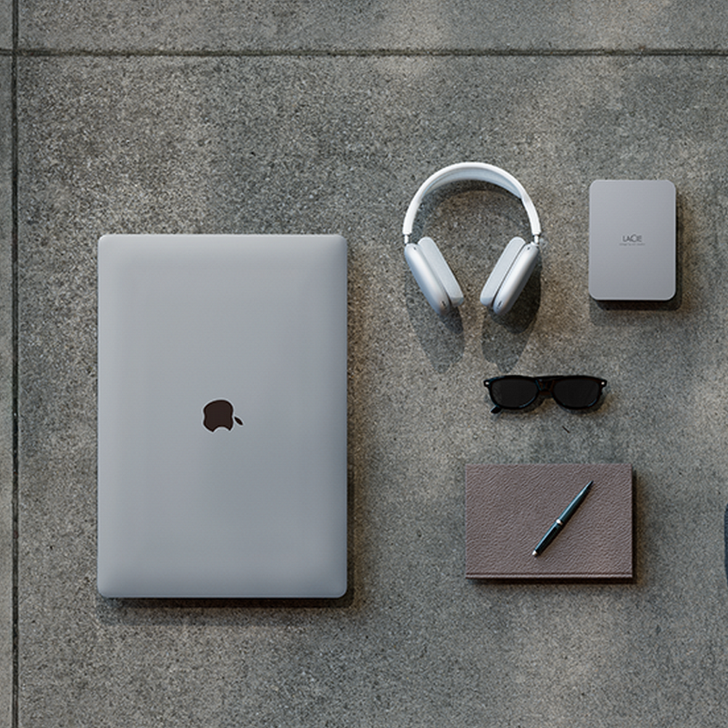 Laptop, słuchawki, okulary przeciwsłoneczne, notatnik i dysk twardy na szarej powierzchni.