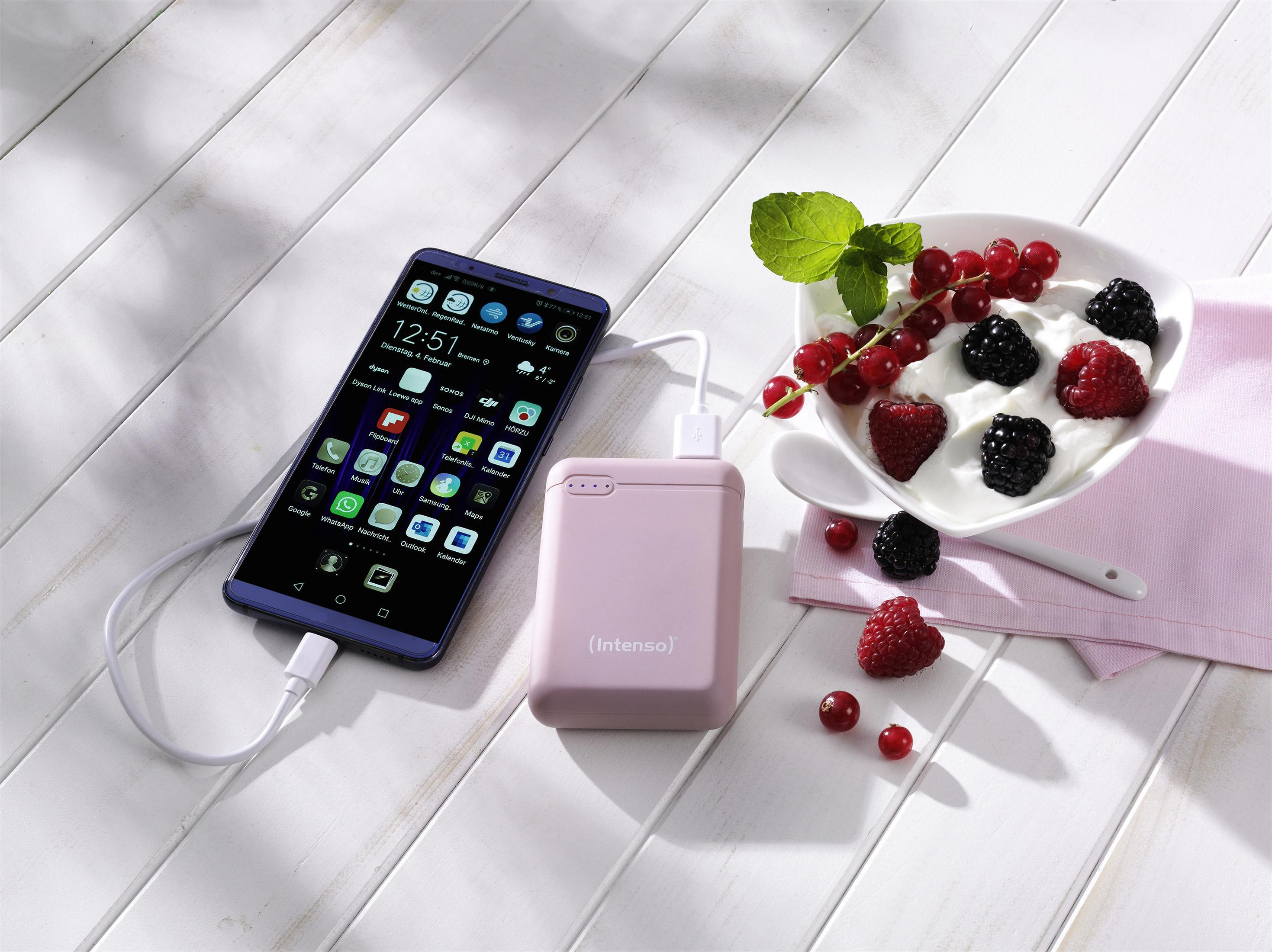 Pinke Powerbank, Smartphone und eine Schüssel Beeren auf einem weißen Tisch. Weißer Hintergrund.