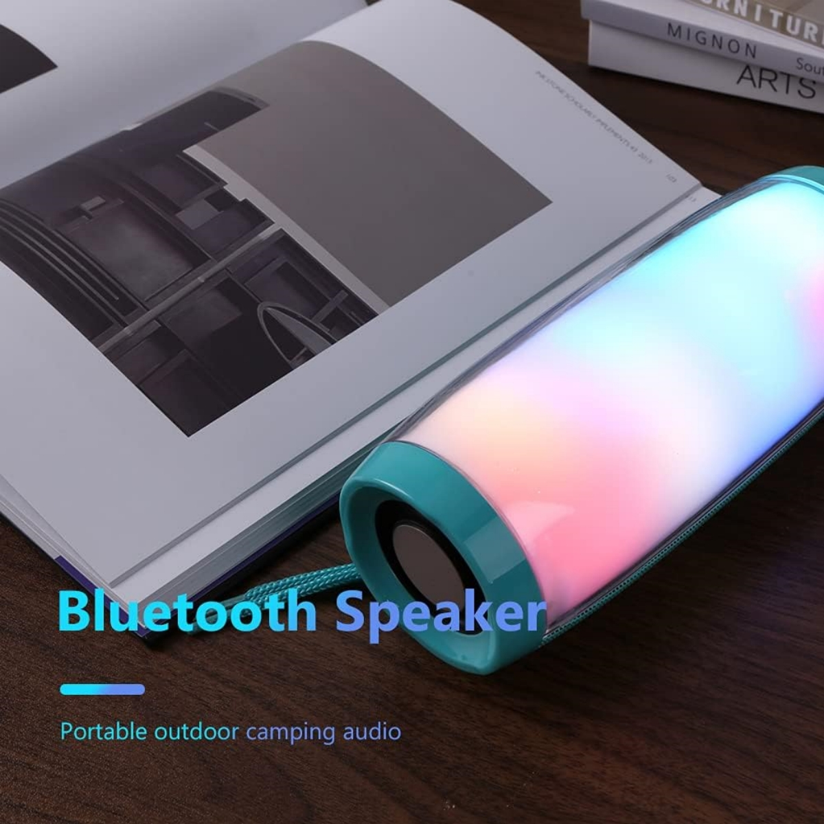 Ein türkisfarbener Bluetooth-Lautsprecher mit mehrfarbigen Lichtern. Er liegt auf einem offenen Buch.