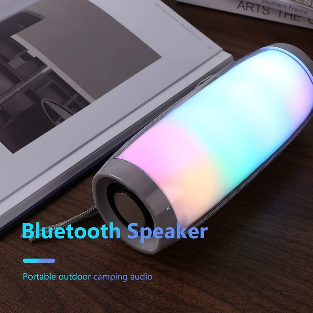 Ein Bluetooth-Lautsprecher mit bunten Lichtern auf einem Holztisch, mit einem Buch im Hintergrund.
