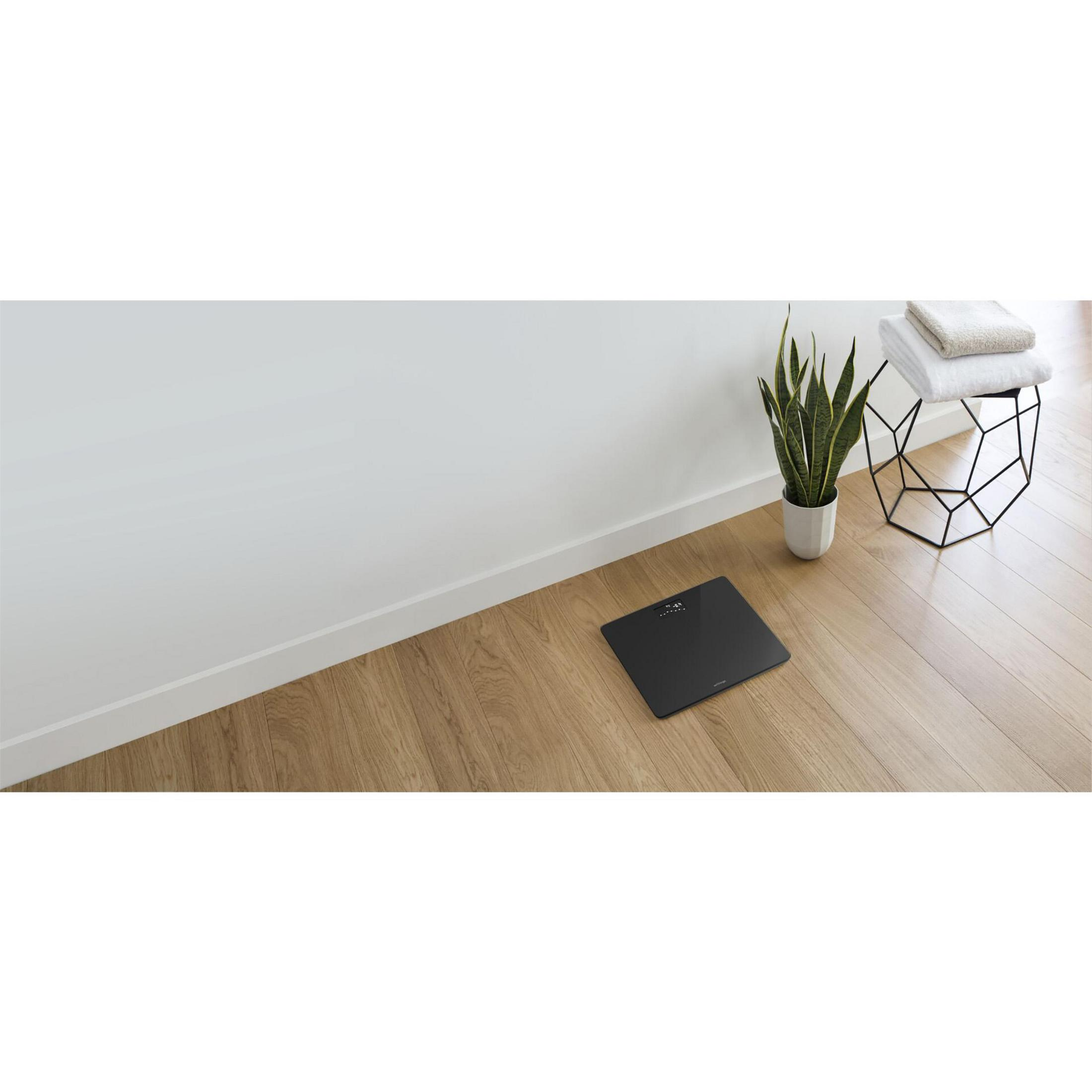 Waga na drewnianej podłodze w pobliżu białej ściany z rośliną i ręcznikami.